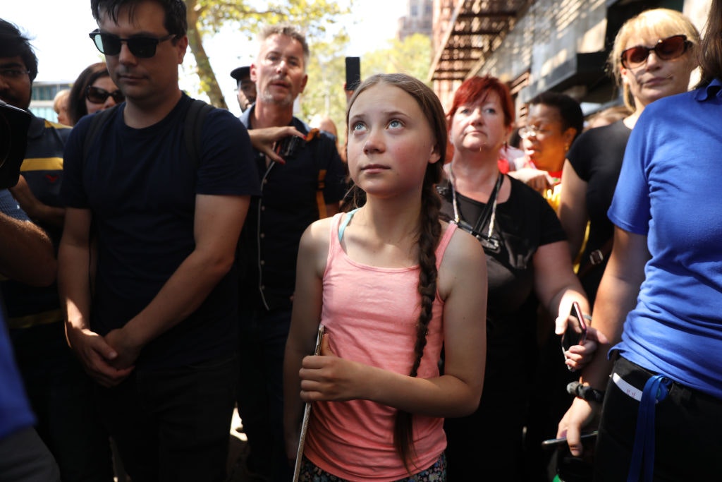 Greta Thunberg walks down the street, surrounded by people and holding a sign. 