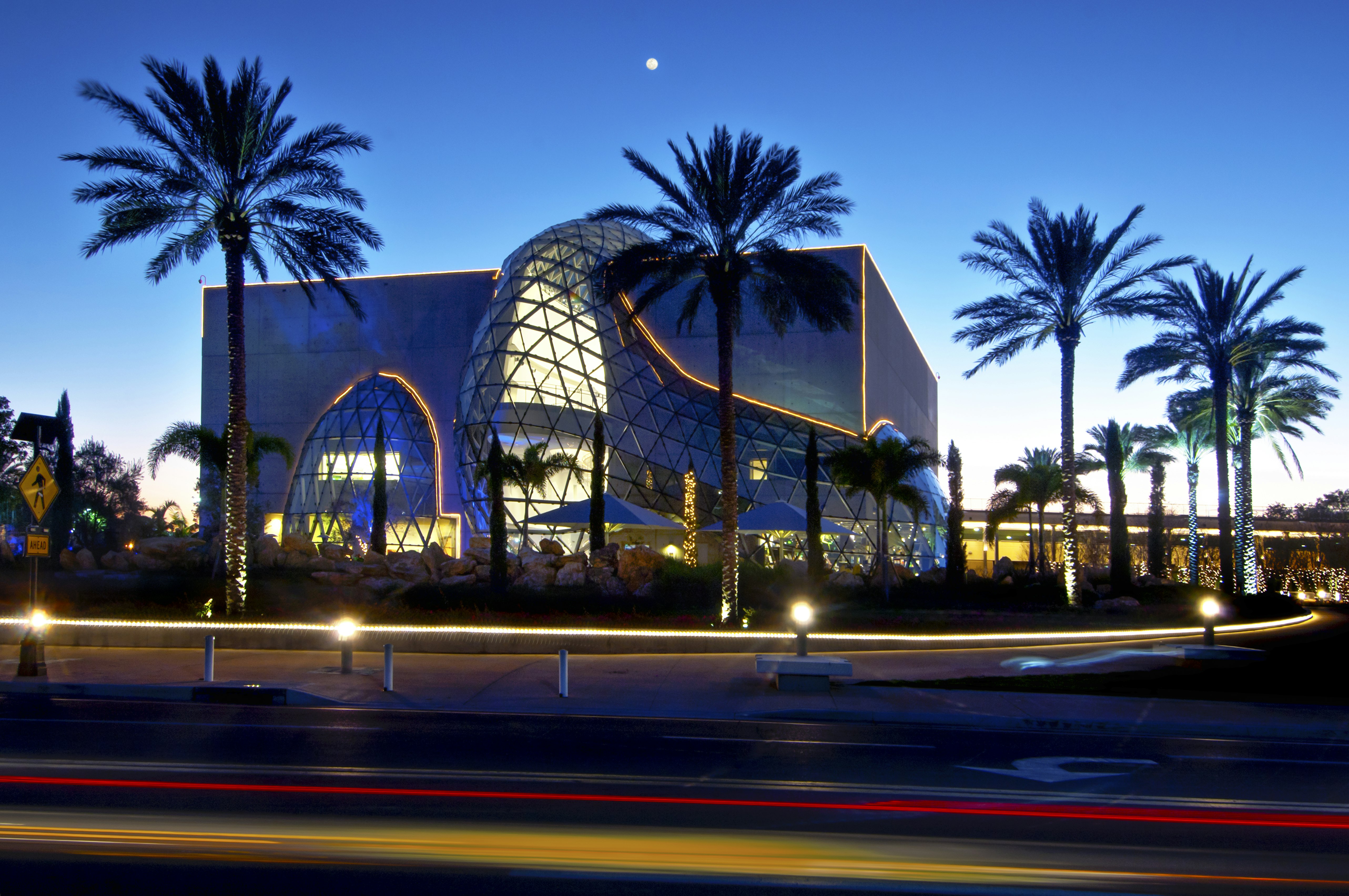 The walls of the Salvador Dali Museum glows a deep cobalt clue against a bright blue summer sky at twilight, a full moon winking over the palm trees surrounding the museum in silhouette