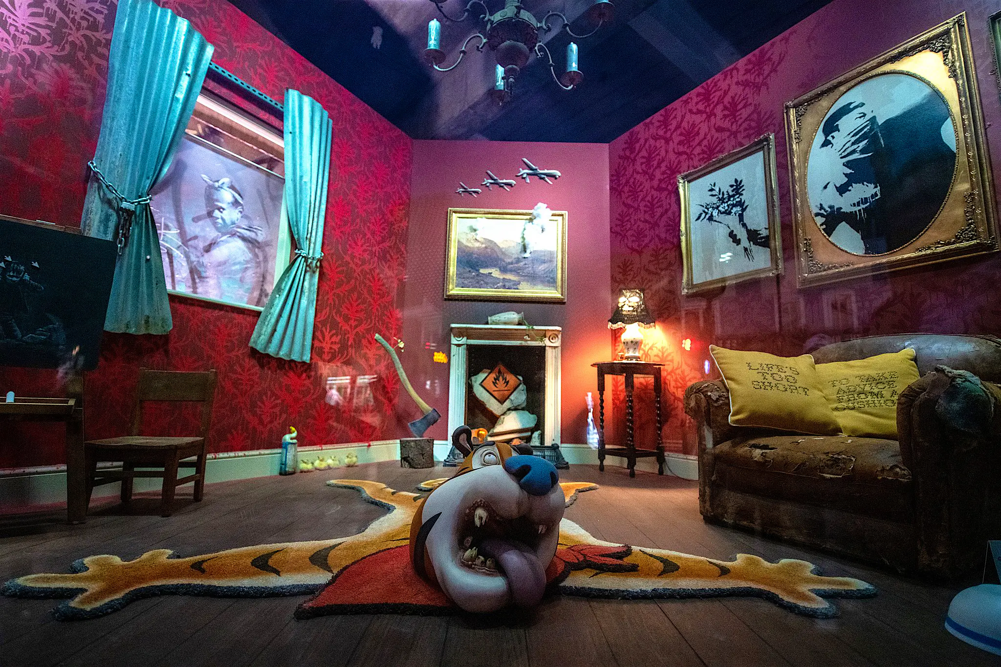 Banksy's "Gross Domestic Product" shopfront A living room with red walls containing a number of unusual objects, including a rug seemingly made from the body of cereal character Tony the Tiger, and an axe sunk into a tree stump.