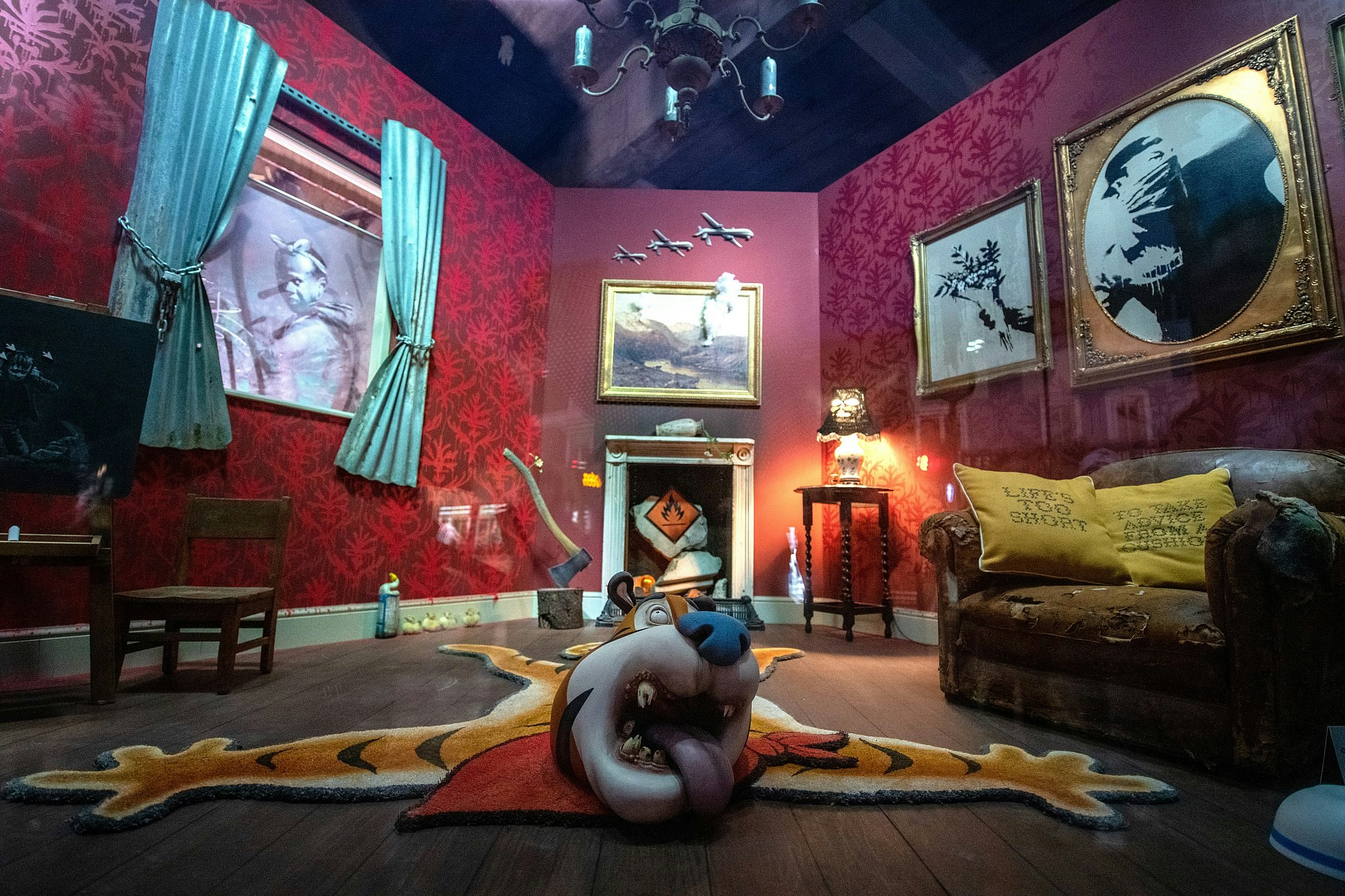 A living room with red walls containing a number of unusual objects, including a rug seemingly made from the body of cereal character Tony the Tiger, and an axe sunk into a tree stump.