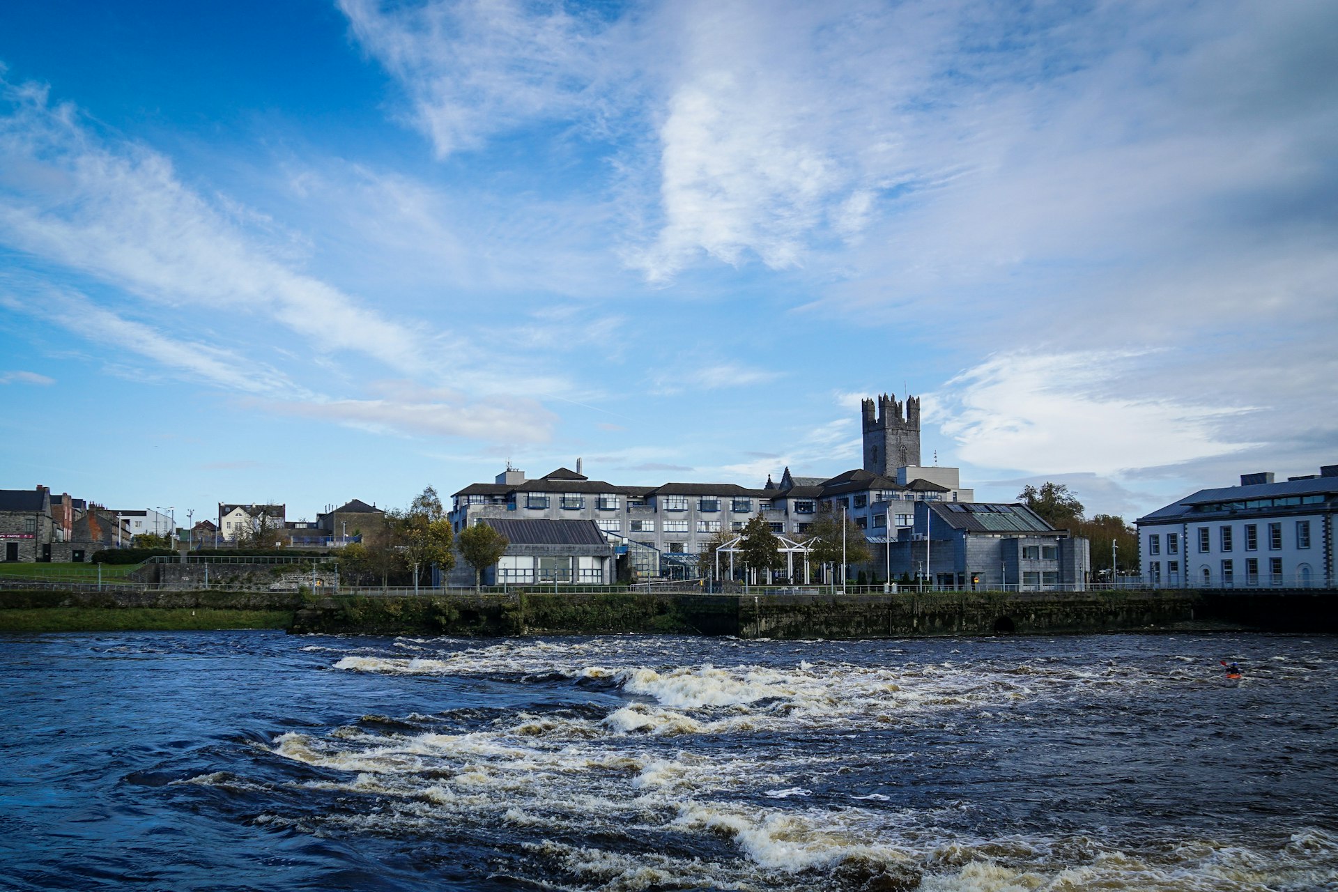 The River Shannon is a deep blue and crested with low, white foamy waves as it laps against the shore where the city and King John's Castle sit