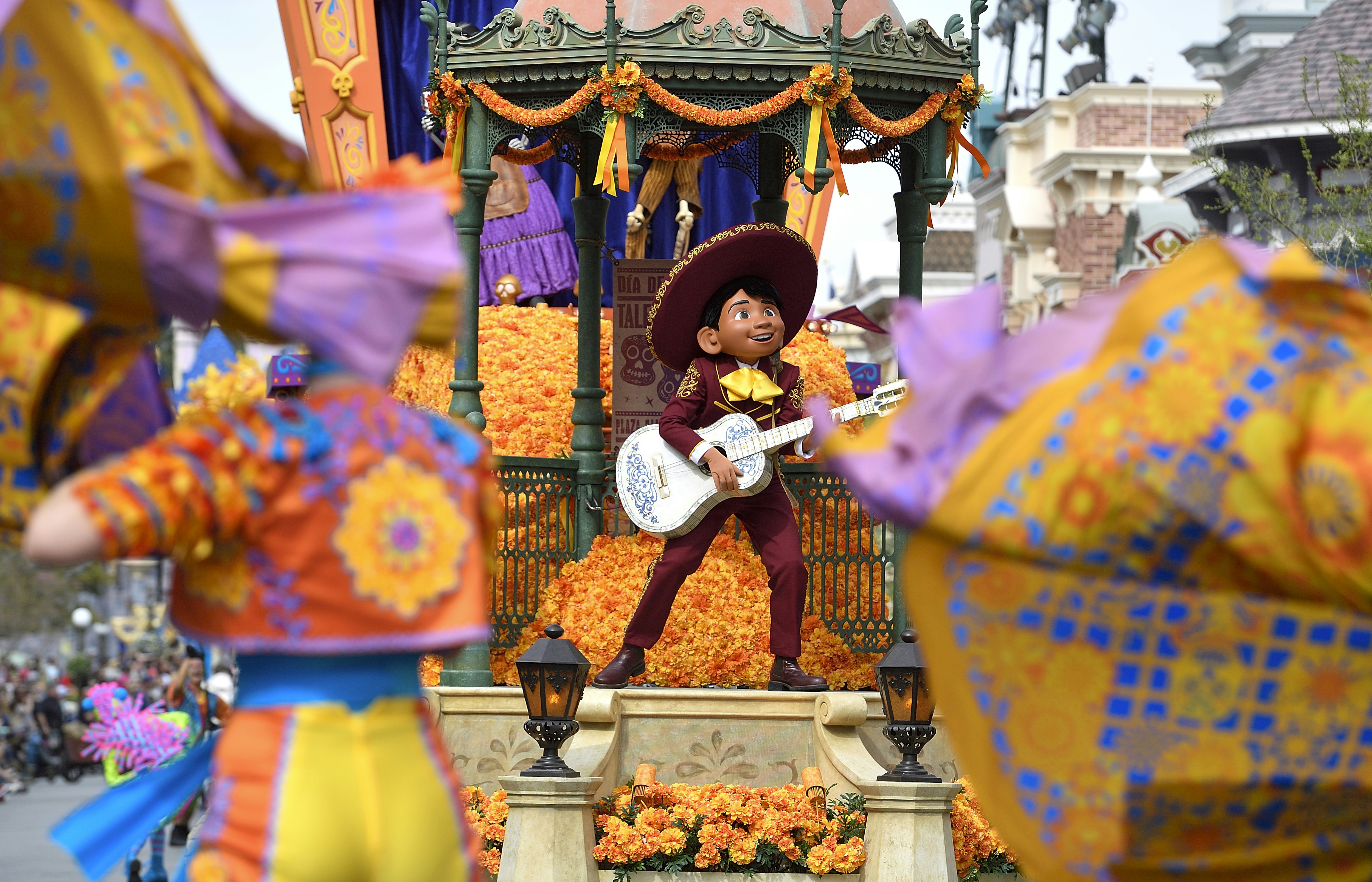 A dressed up character plays the guitar on a colorful parade float