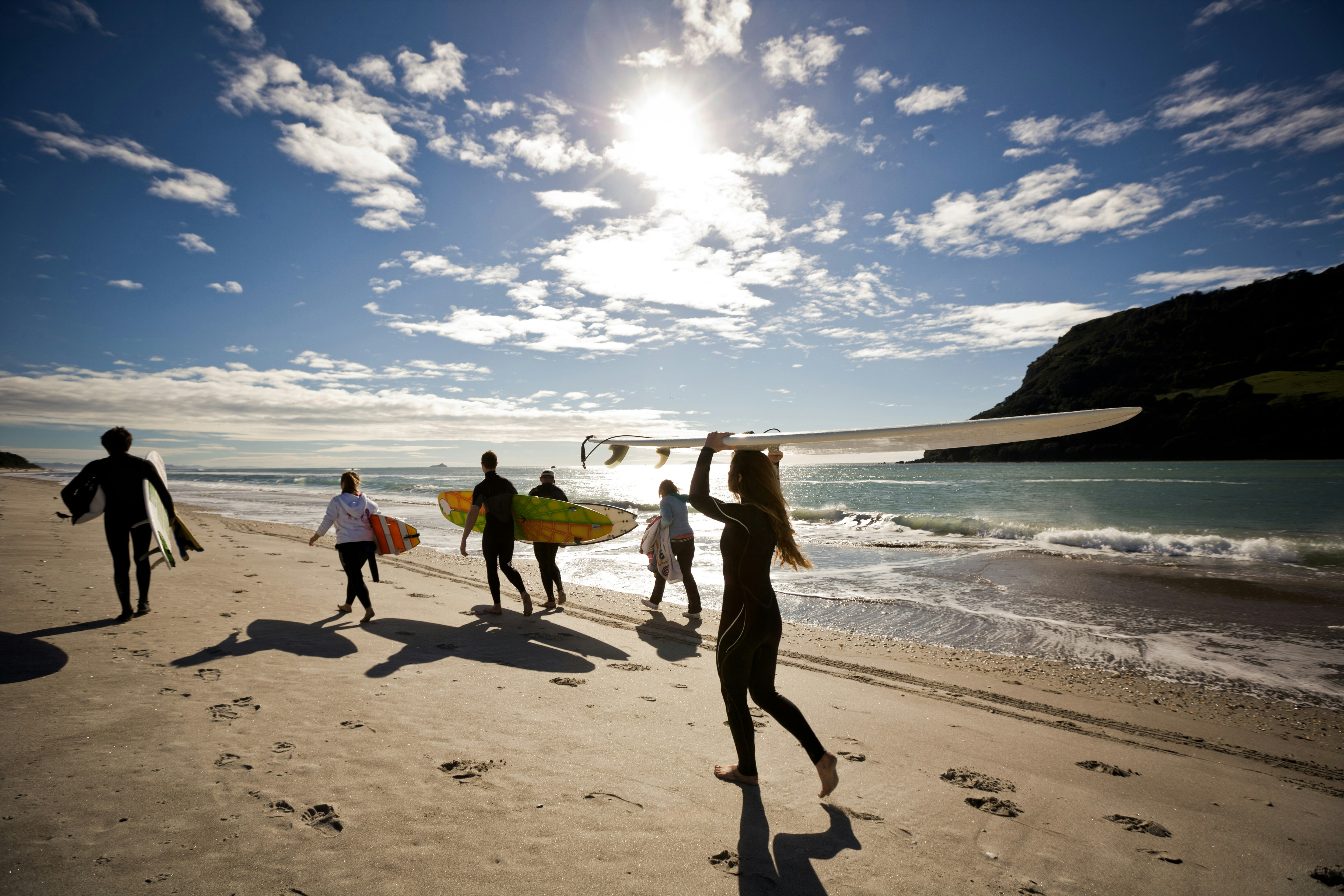 People in wetsuits running down the beach in New Zealand with surfboards; Where to travel with your tweens and teens