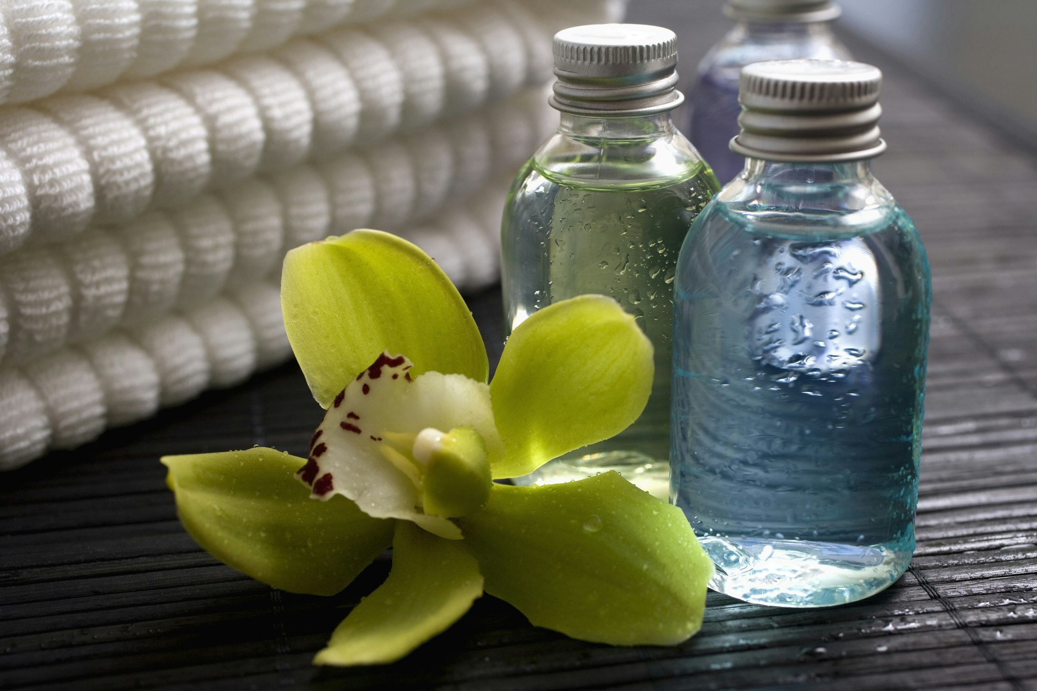 Two mini plastic bottles of clear liquid lined up beside towels and a flower