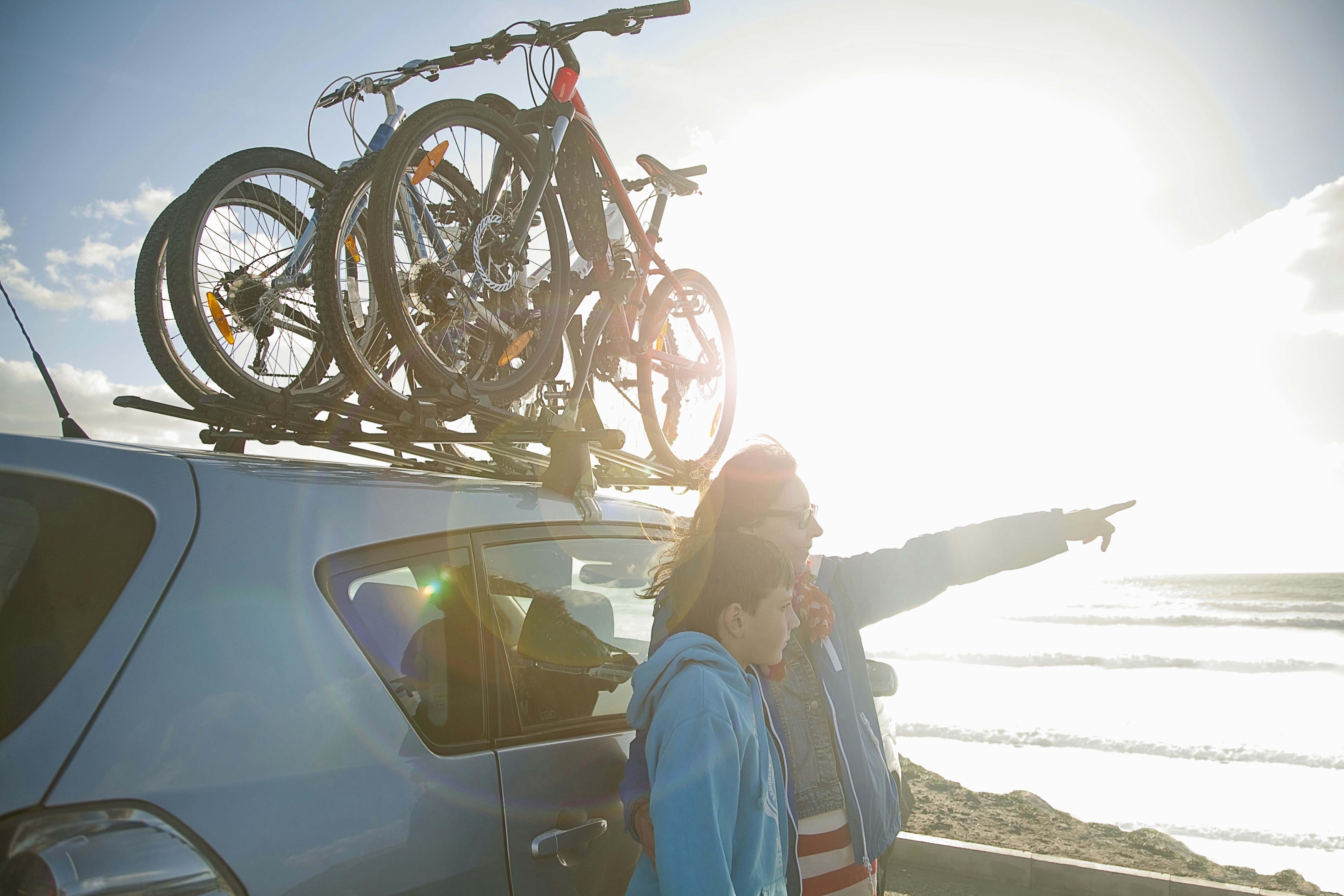 Mother and son overlooking beach, standing by car with bikes on the rack