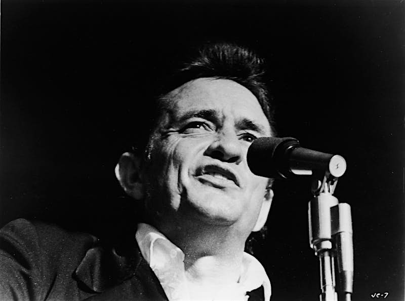 Black and white photo of Johnny Cash from the shoulders up, singing into a mic at a show