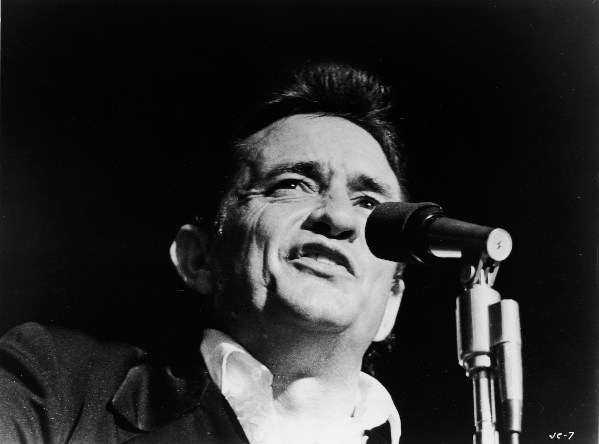 Black and white photo of Johnny Cash from the shoulders up, singing into a mic at a show