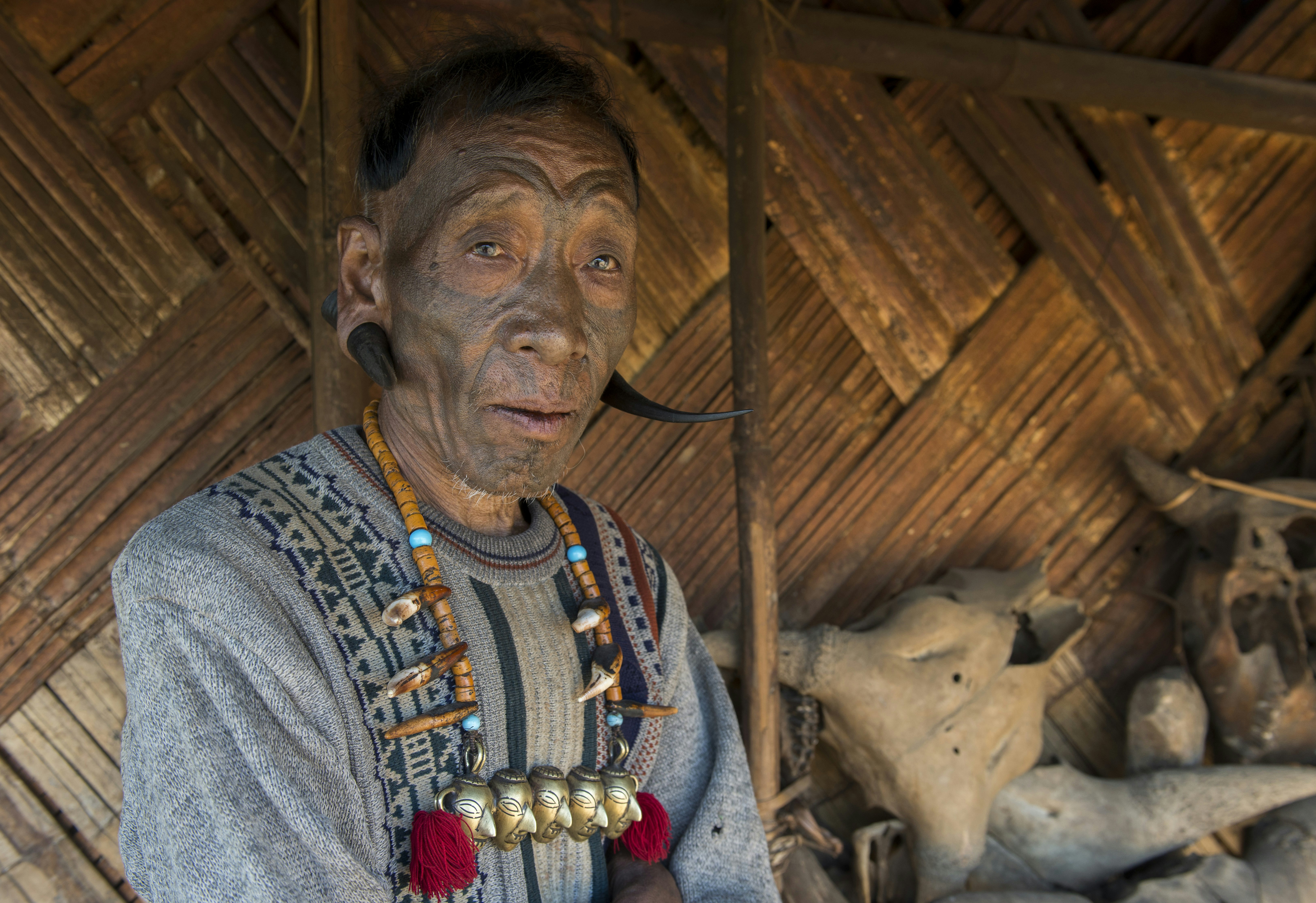 Profile shot of a former headhunter from the Konyak tribe in Nagaland. The man's face is darkened by tattoo ink and he has two large black tusks piercing either ear.