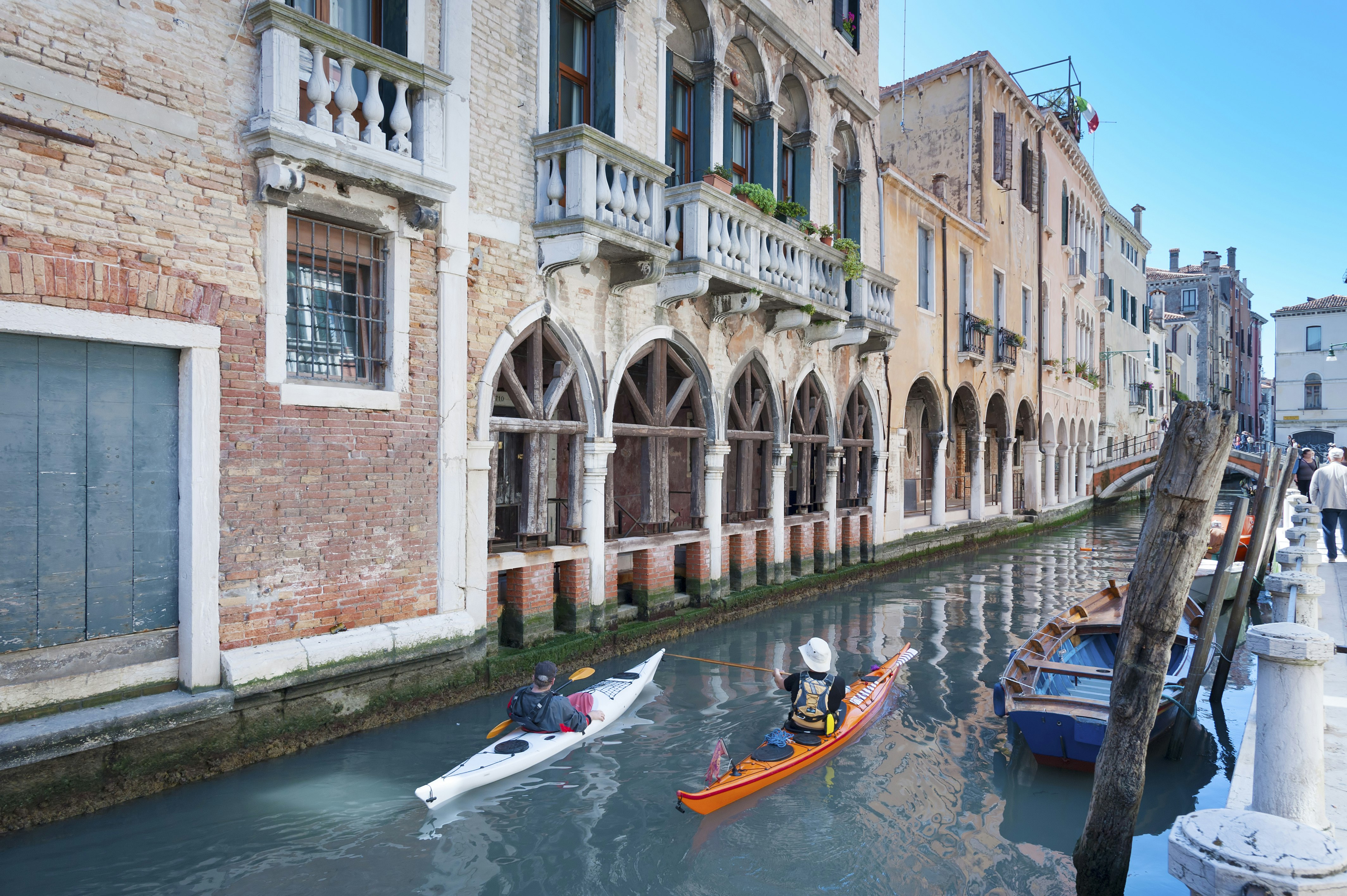 Two people steer their kayaks along a canal in Certosa, Venice