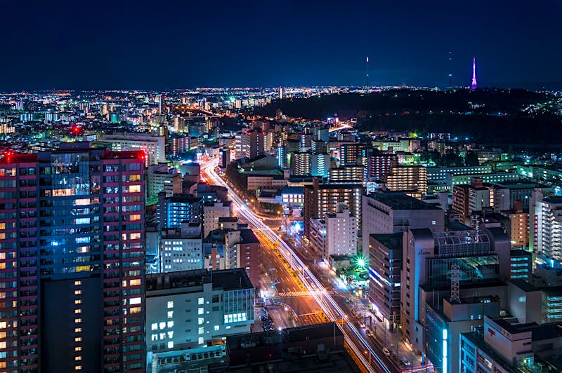 An aerial view of the city of Sendai at night, with the streetlights and interiors of tower blocks illuminating the large city.
