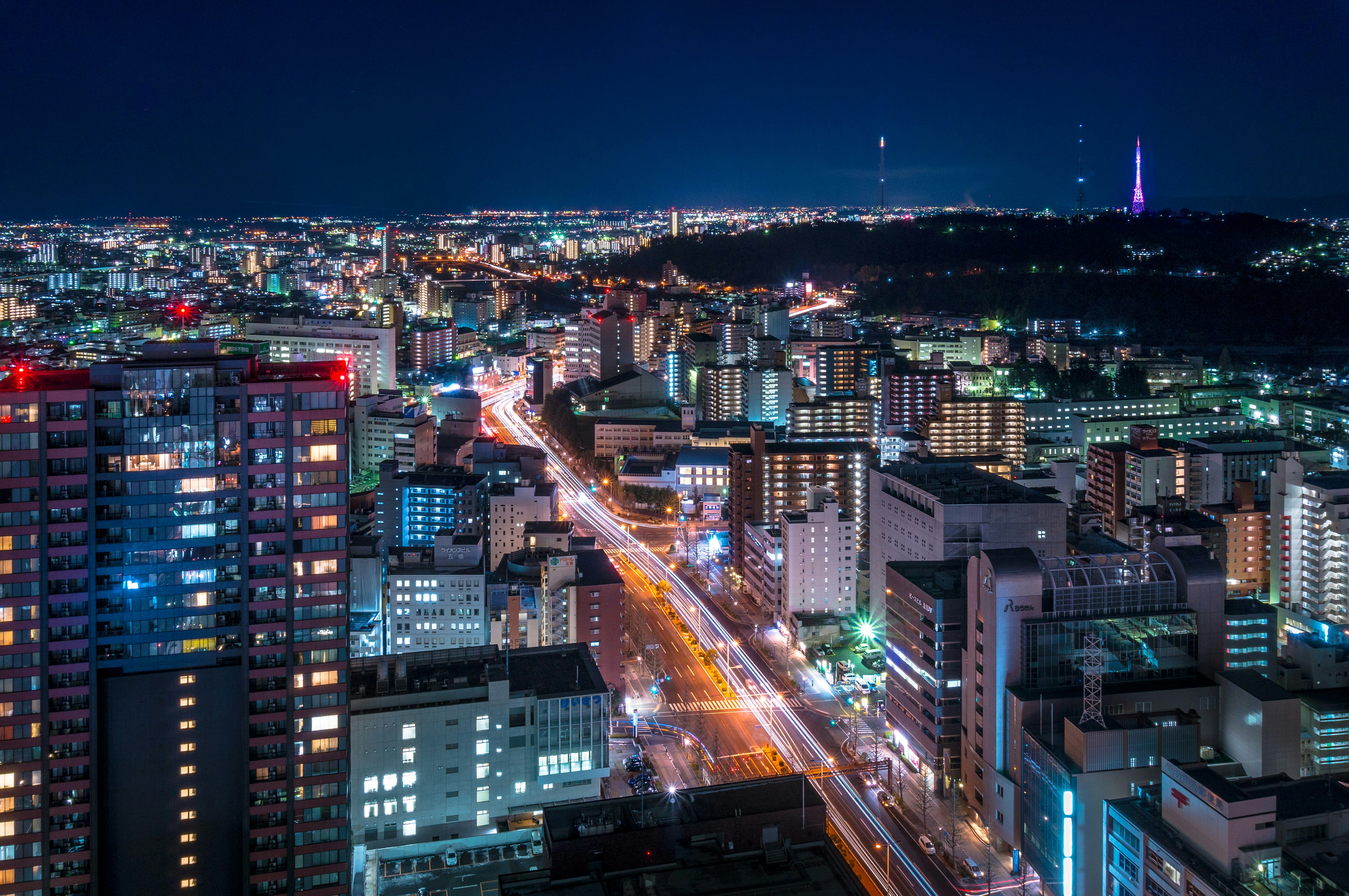 An aerial view of the city of Sendai at night, with the streetlights and interiors of tower blocks illuminating the large city.