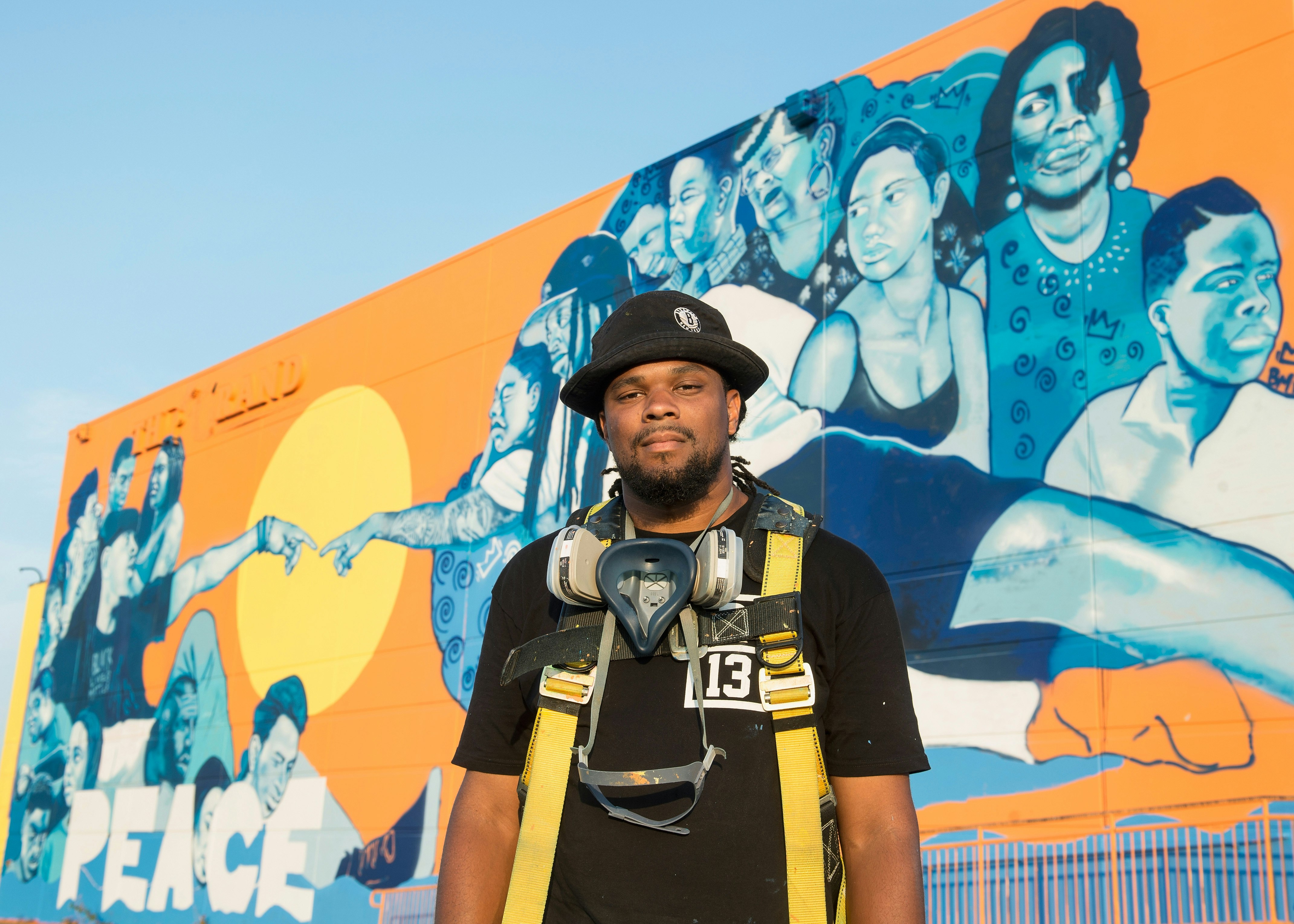 Brandan Odums or BMike stands in front of the Wall of Peace Mural which he paineted