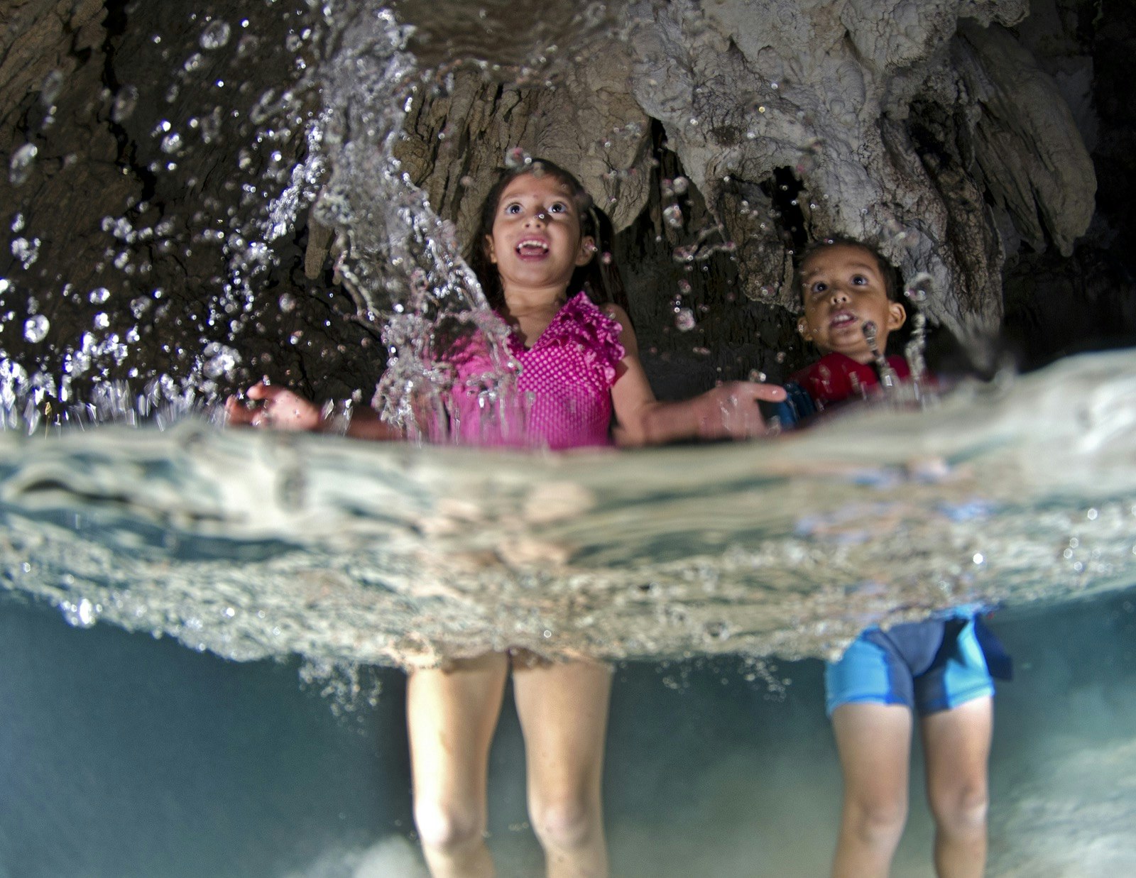 Two kids in bathing suits and life jackets stand in shallow water in a cave in Tulum Mexico