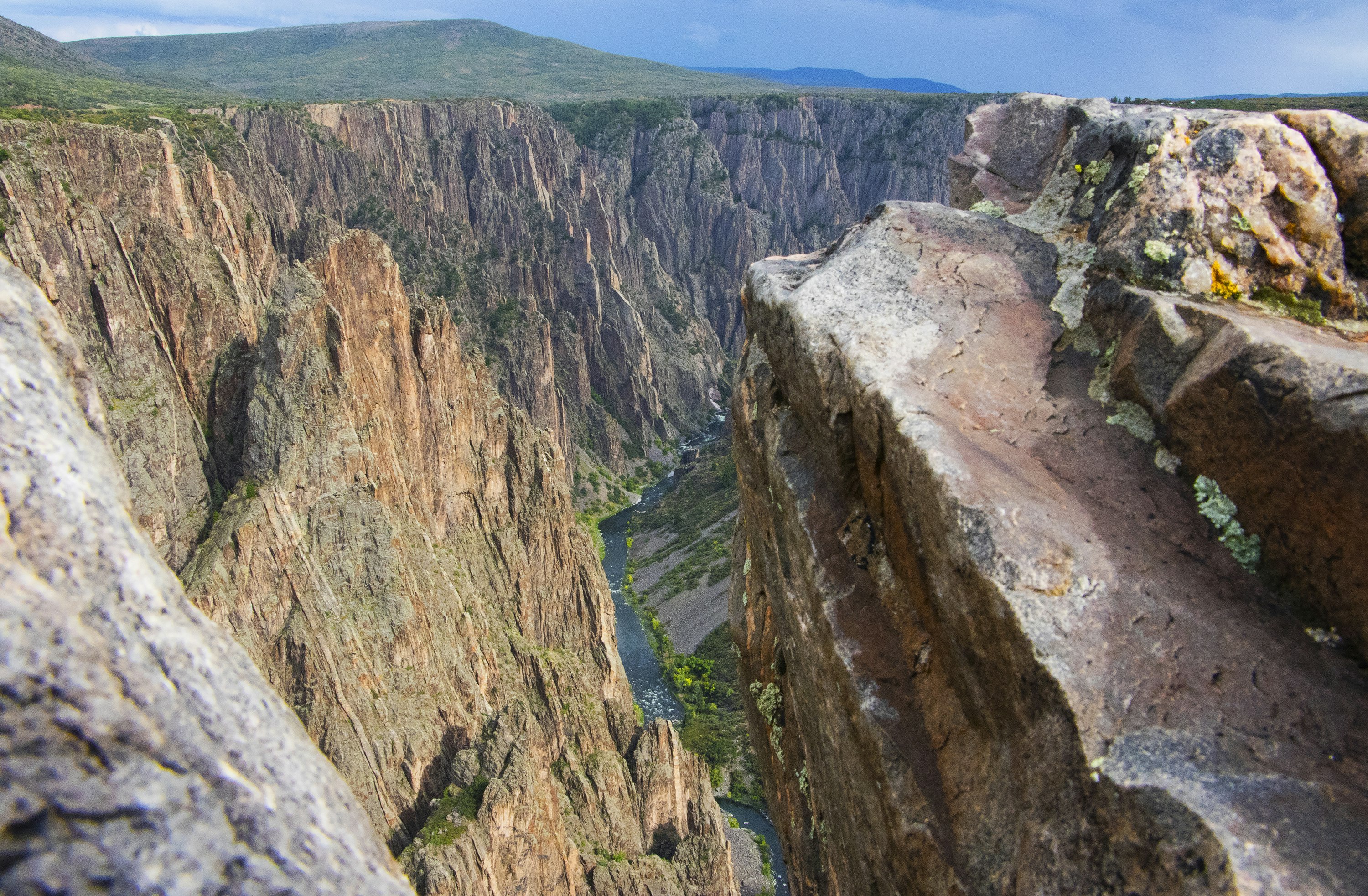 A narrow blue ribbon of water cuts through tall walls of sheer grey stippled rock in Black Canyon of the Gunnison National Park