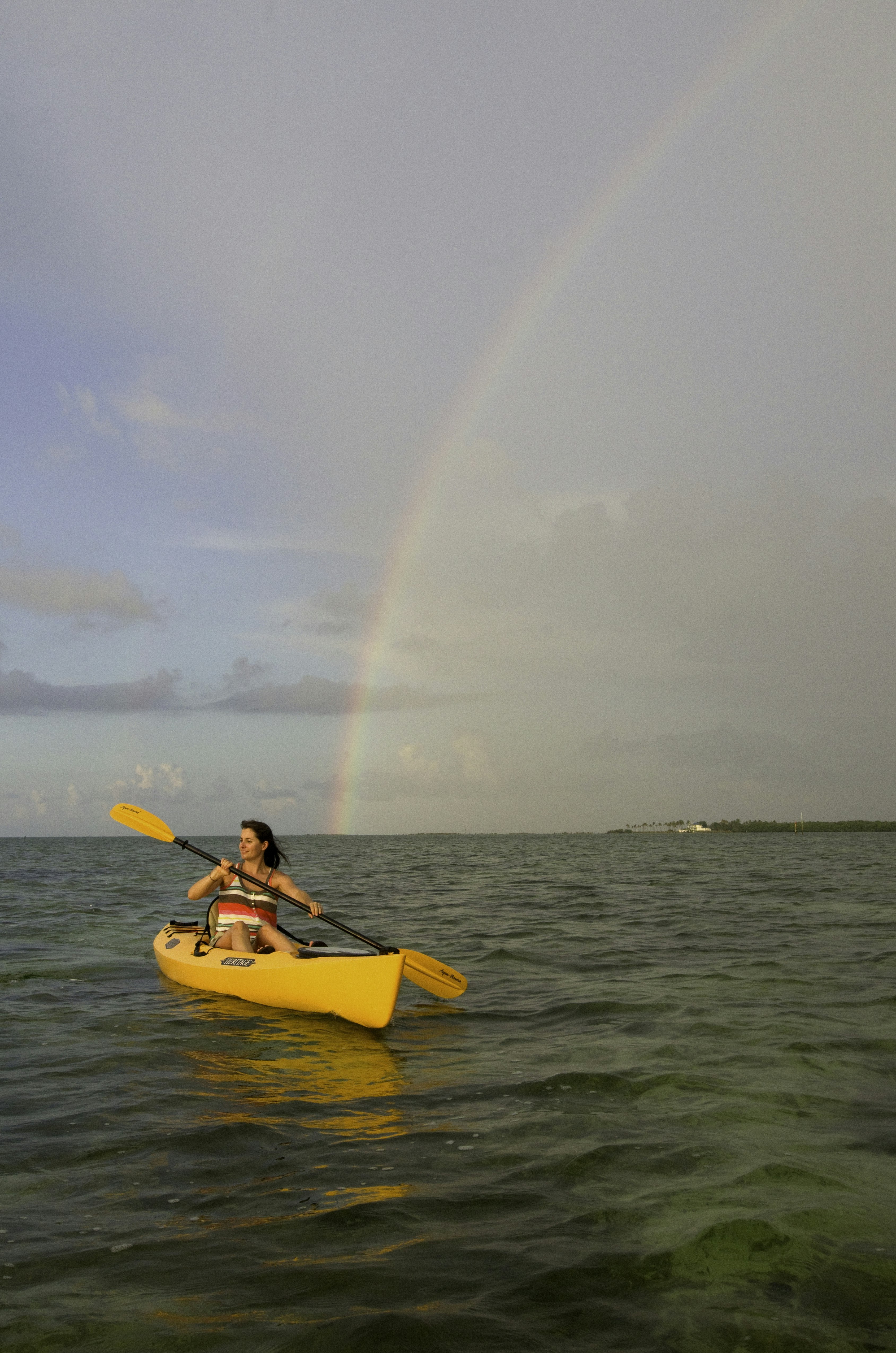 A woman paddles a kayak on the sea off Islamorada, Florida, as a rainbow lights up the morning sky behind her