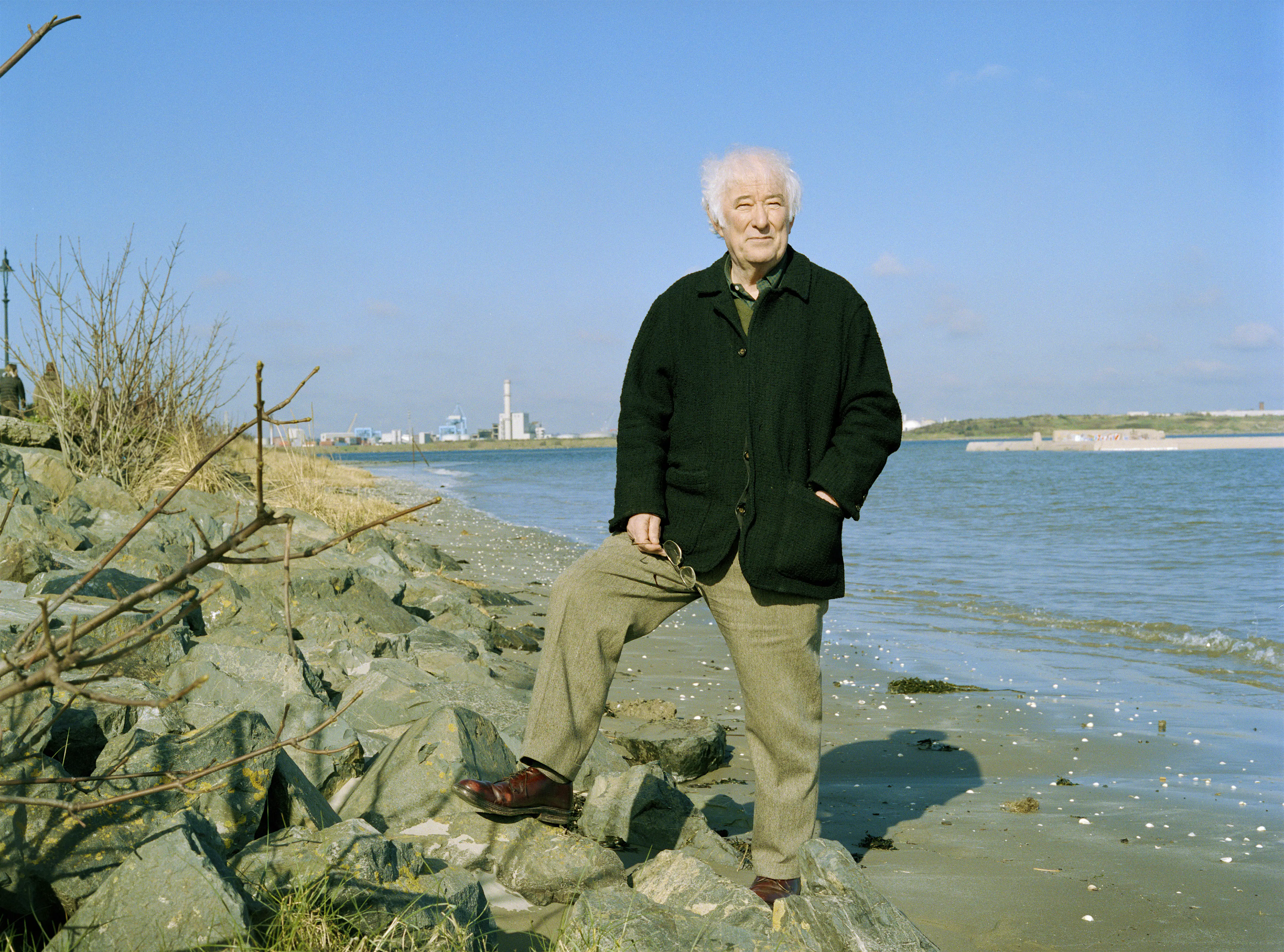 seamus-heaney.jpg Nobel-prize winning poet Seamus Heaney stands on the Irish coast in tweed slacks, dark brown leather shoes, and a black coat, holding his glasses in his right hand. His left is in his coat pocket.