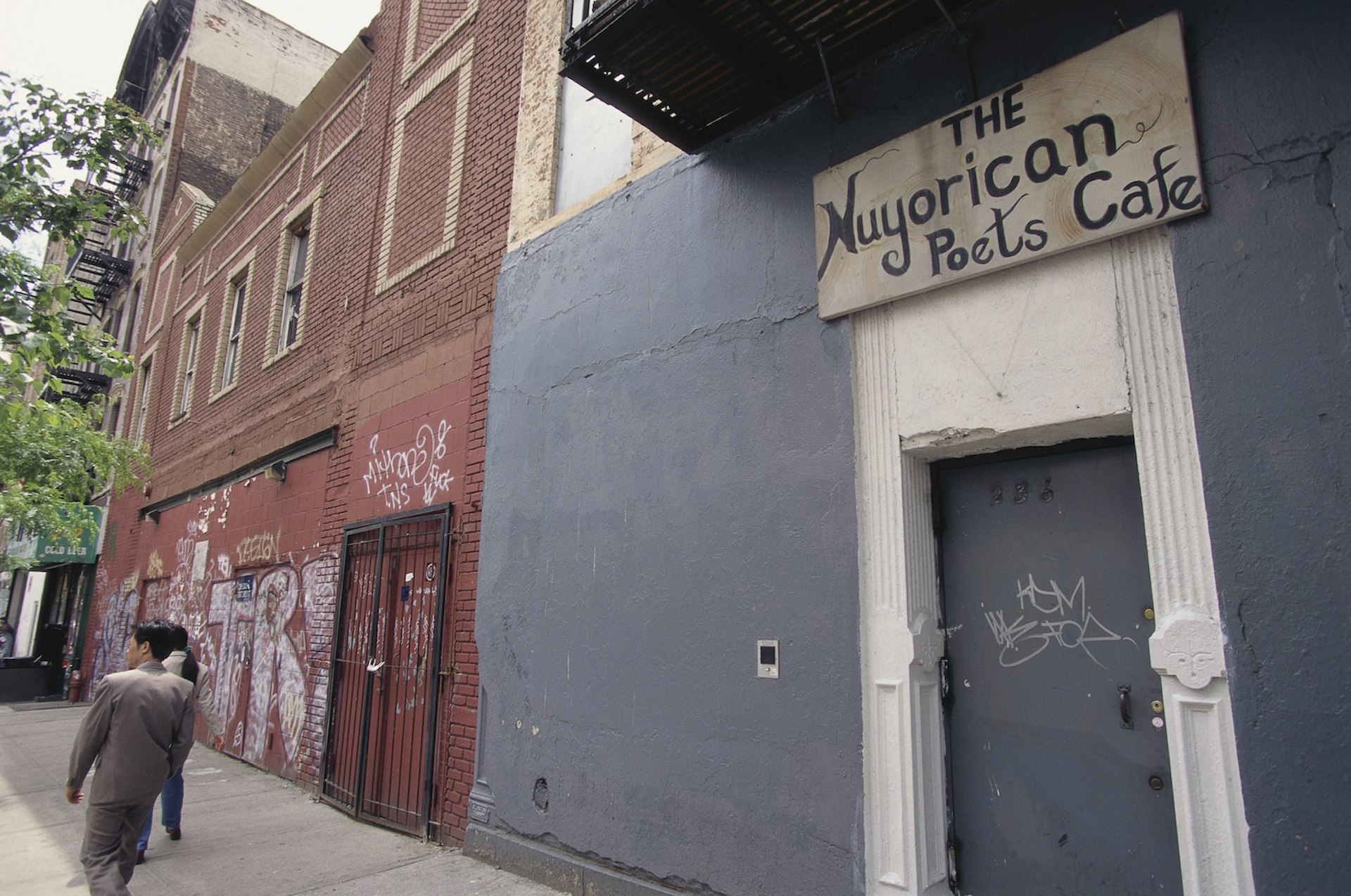 A gray door, gray wall, and wooden sign reading "Nuyorican Poets Cafe"