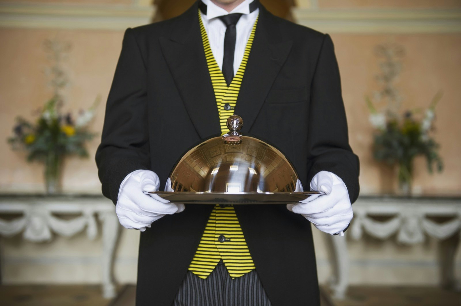 A butler holding a silver tray with a silver cloche on it
