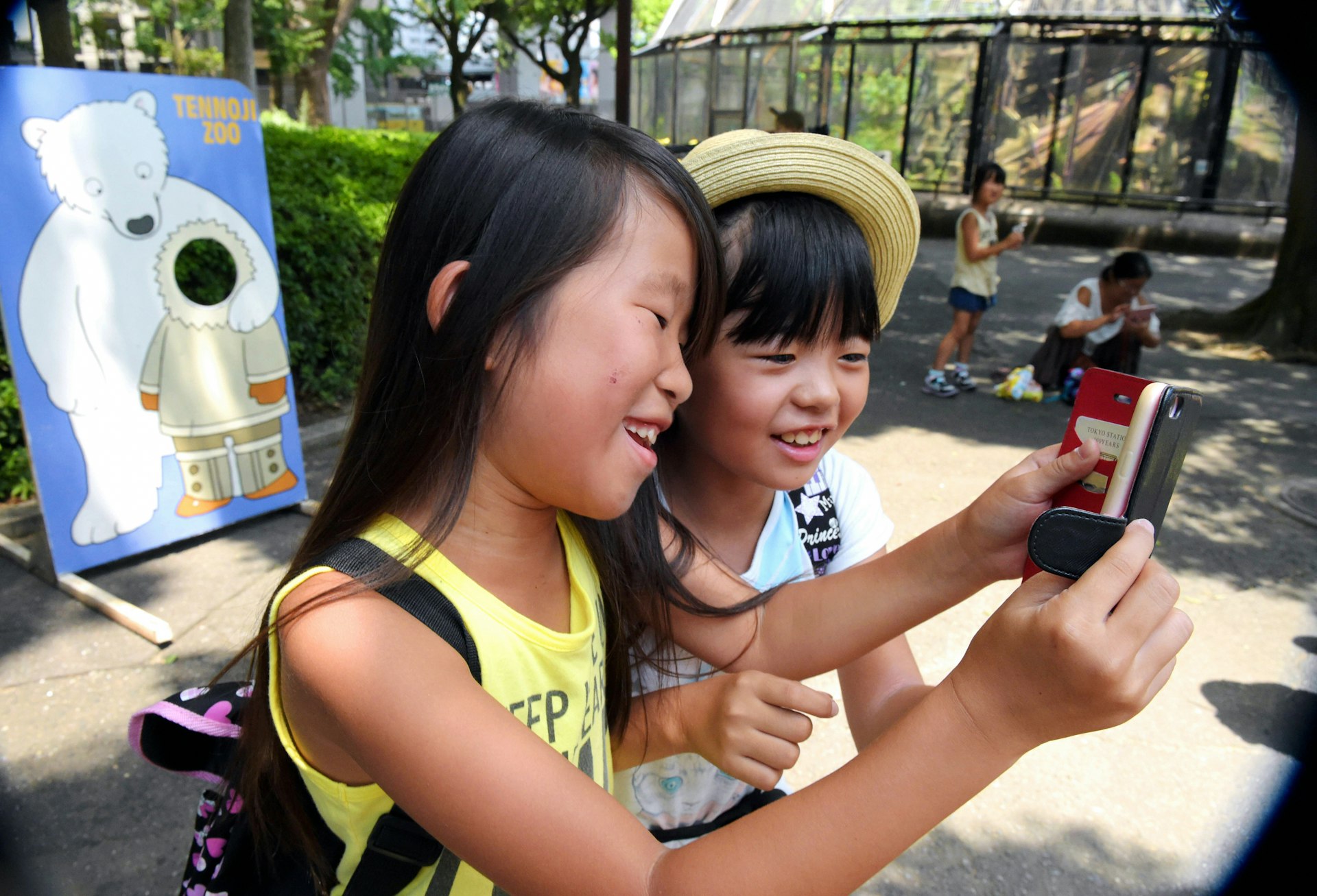 Two children smile as they hold up a mobile phone. There's a cut-out of a polar bear in the background, labelled Tennoji Zoo