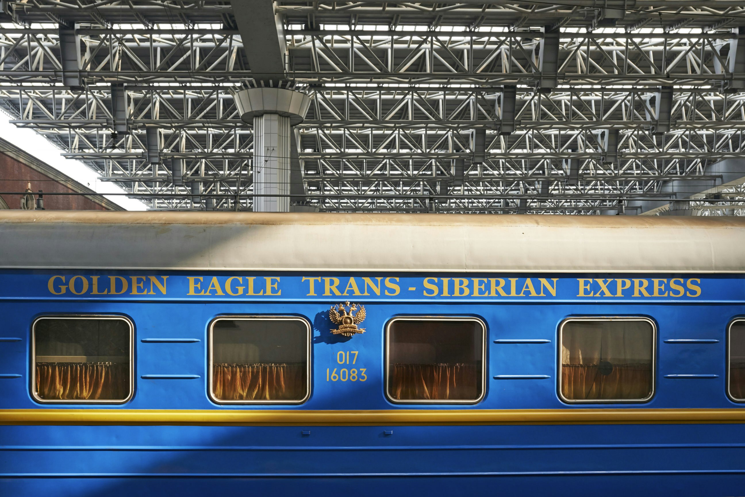 A bright blue vintage train carriage sitting in a covered train station; gold-coloured on the train states 'Golden Eagle Trans-Siberian Express'.