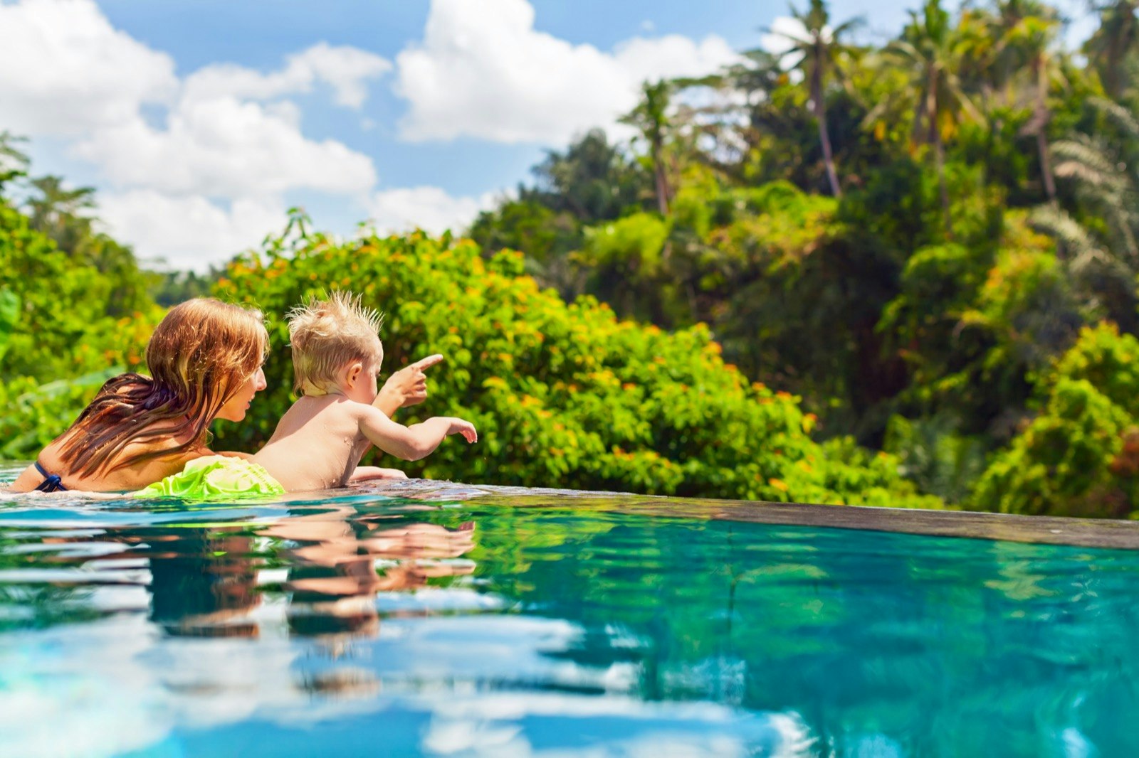 A mother and her son point to something off in the jungle on the edge of an infinity pool in Bali, Indonesia
