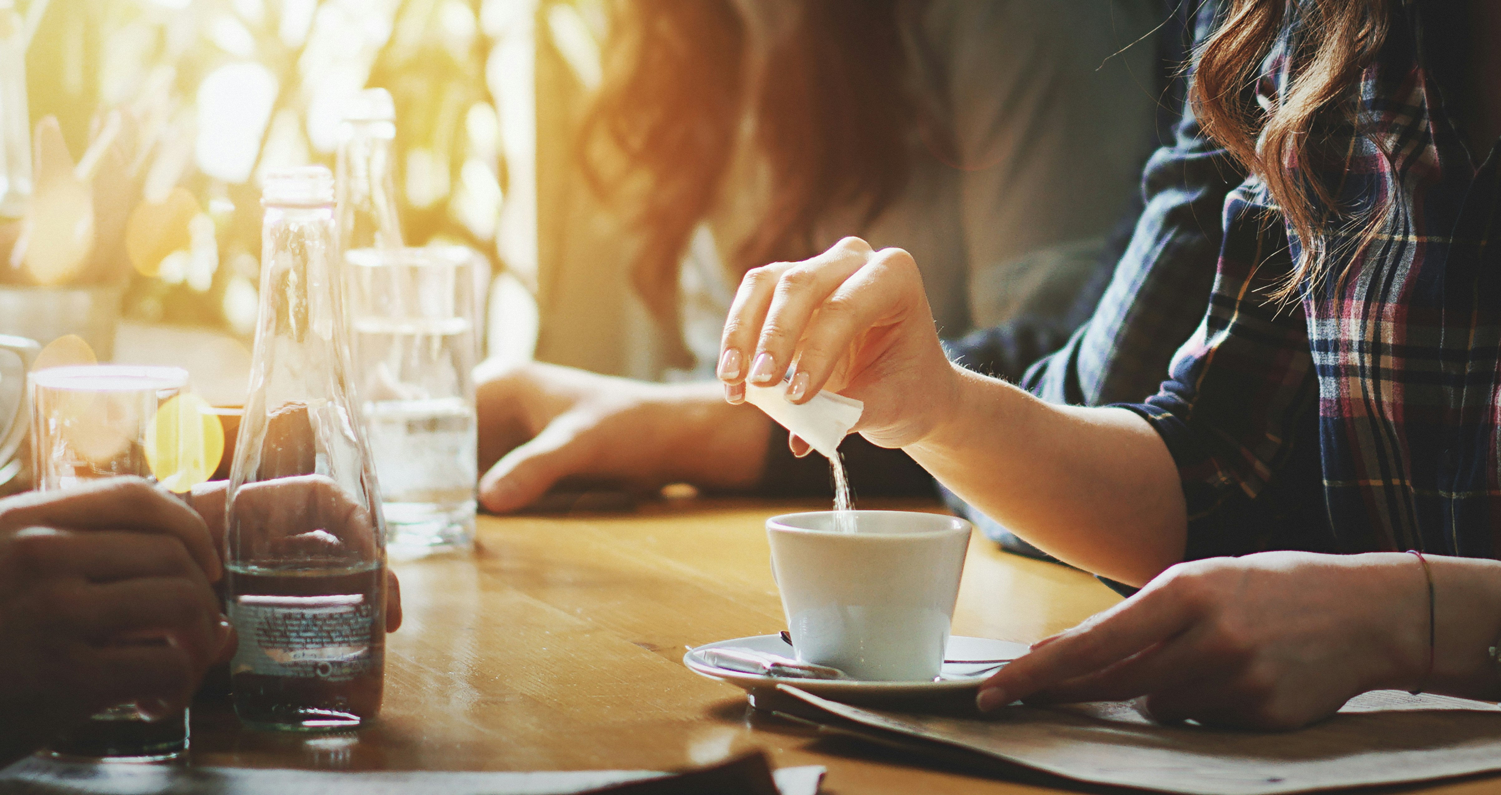 En kvinna häller en påse socker i en kopp kaffe.