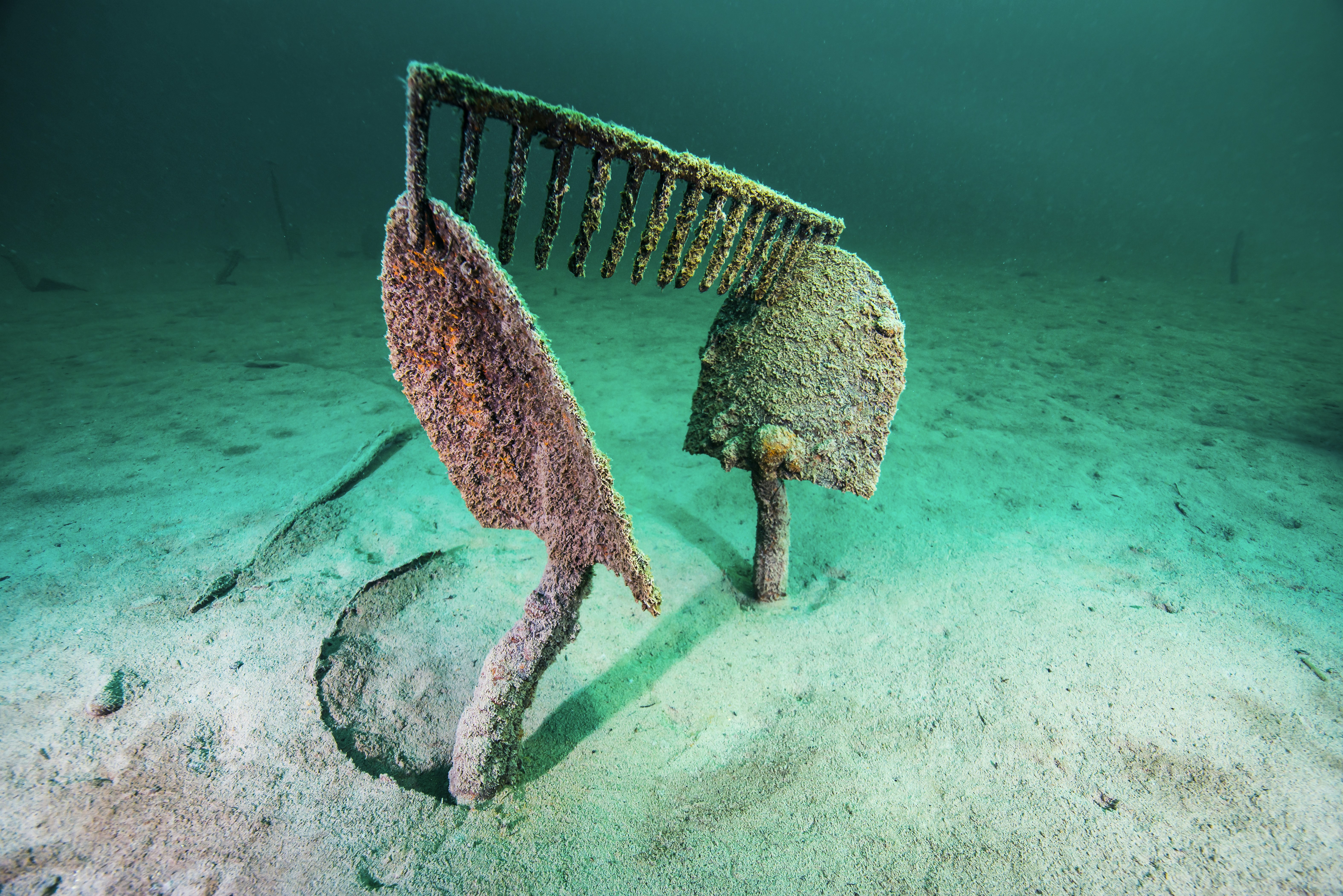 Two shovels, rusted and covered in marine sediment, stand straight up from the bed of Lake McDonald, with an equally rusted rake head perched on top. All around are the deep teal and bright aqua waters found throughout Glacier National Park