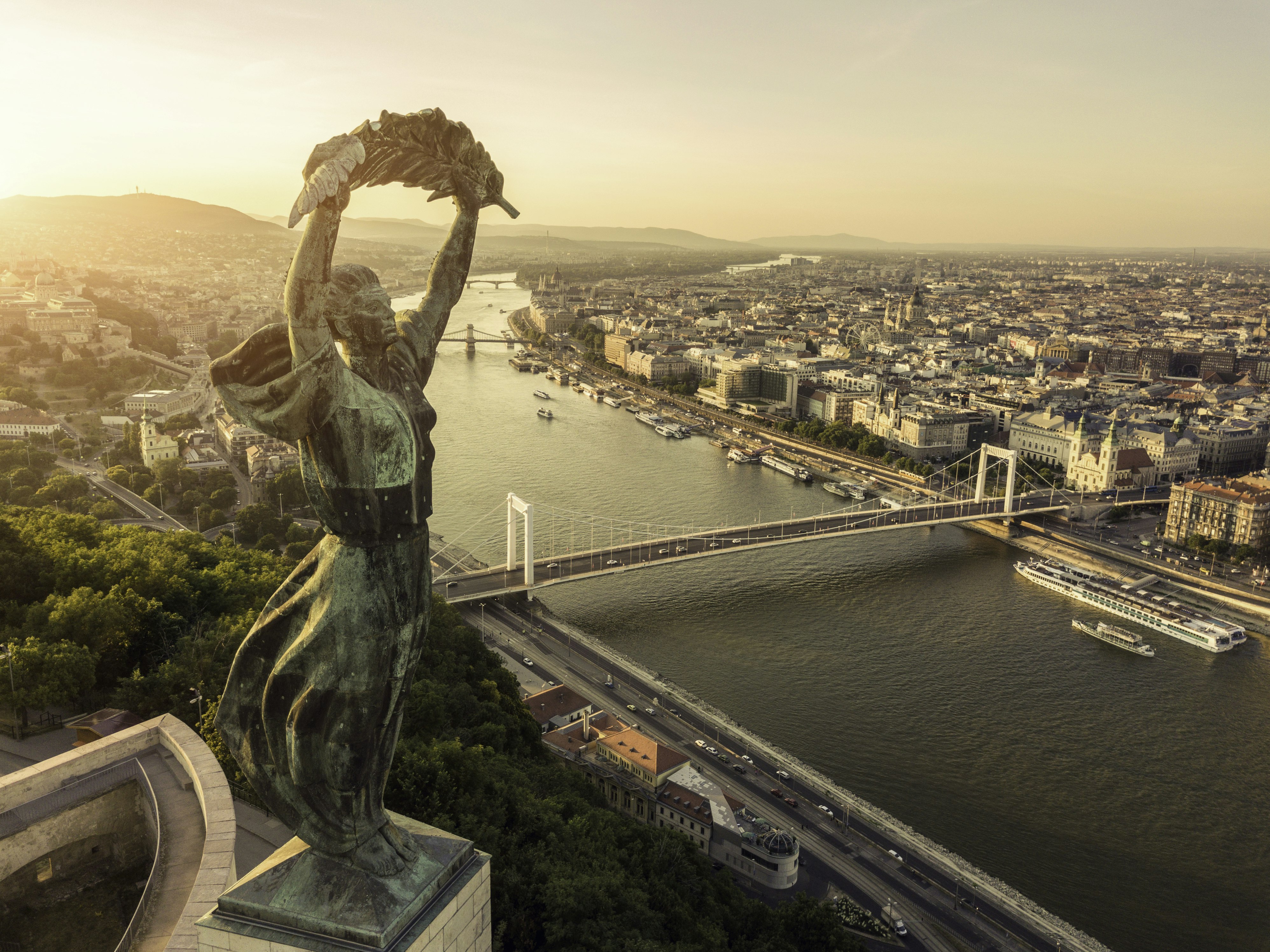 Aerial view of Budapest cityscape and Liberty Statue under a golden sky