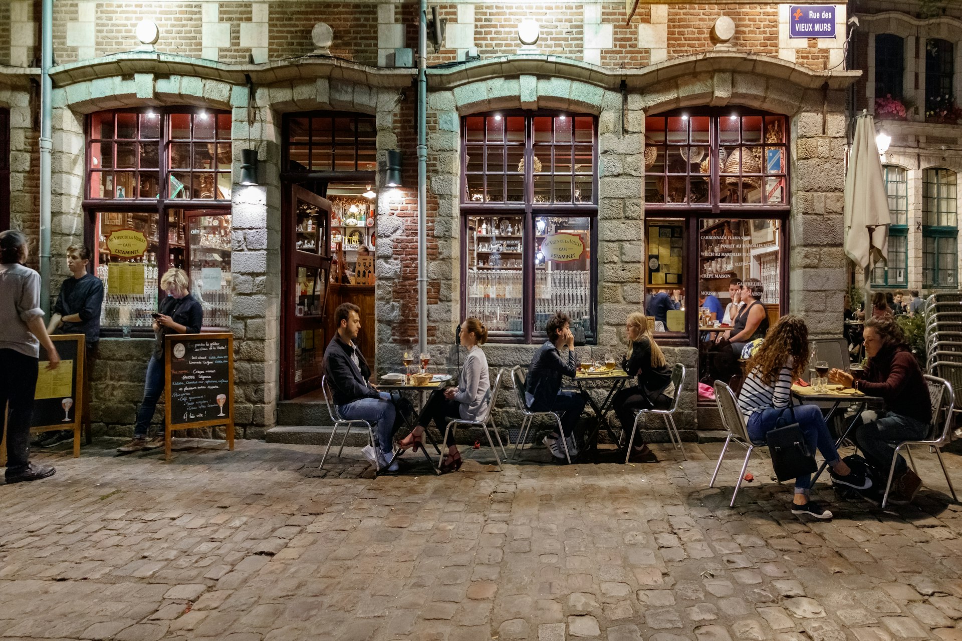 People sitting at tables outside a traditional bar in a historic building with a brick and stone facade.