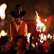 An effigy of a man wearing a wide-brimmed black hat is high above a crowd of people parading through the streets. There are several flaming torches and flags on display as Lewes Bonfire Society celebrates Bonfire Night