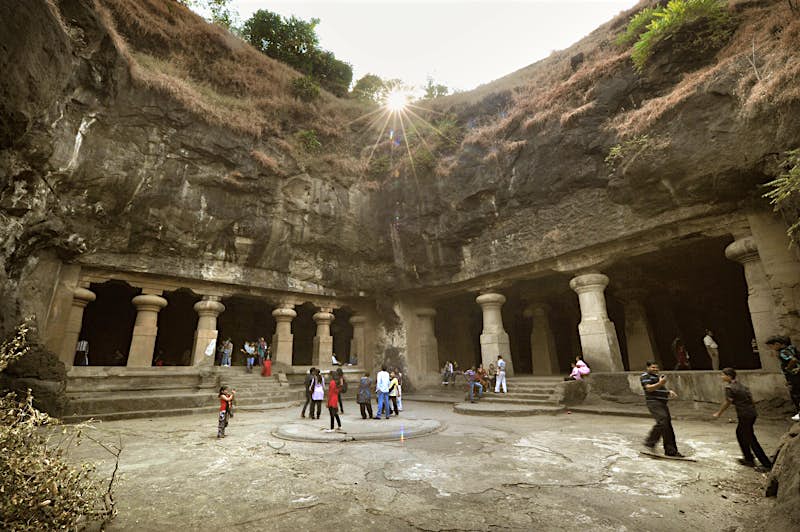 Groups of visitors wander around the Elephanta Cave complex in Mumbai. The complex includes several open-air 'courtyards', as shown here, with the sunlight shining down from above.