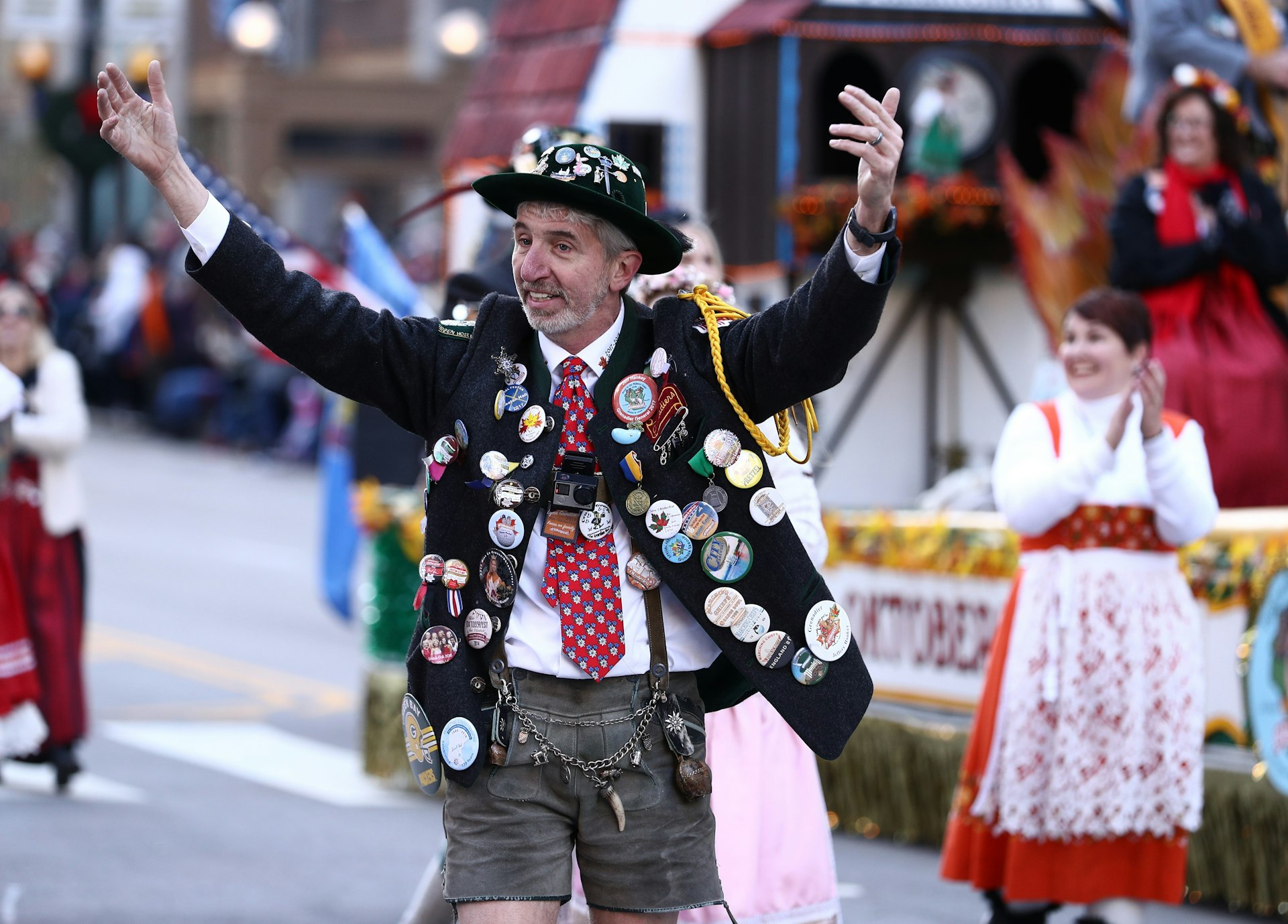 A man covered in buttons and badges raises his arms during a Thanksgiving Day parade