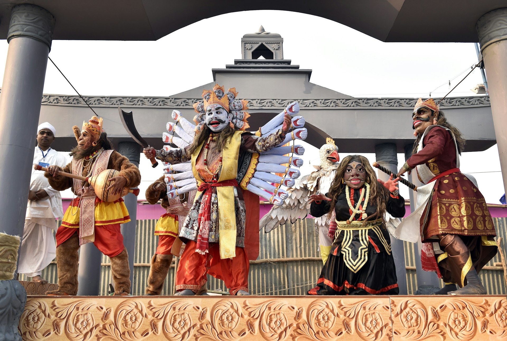 A group of people from Assam perform a traditional dance show wearing colourful masks and outfits resembling Hindu deities.