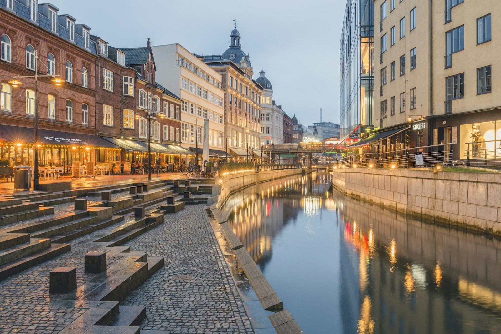 The city of Aarhus is lit up on each side of the canal as dusk falls; Copenhagen alternatives