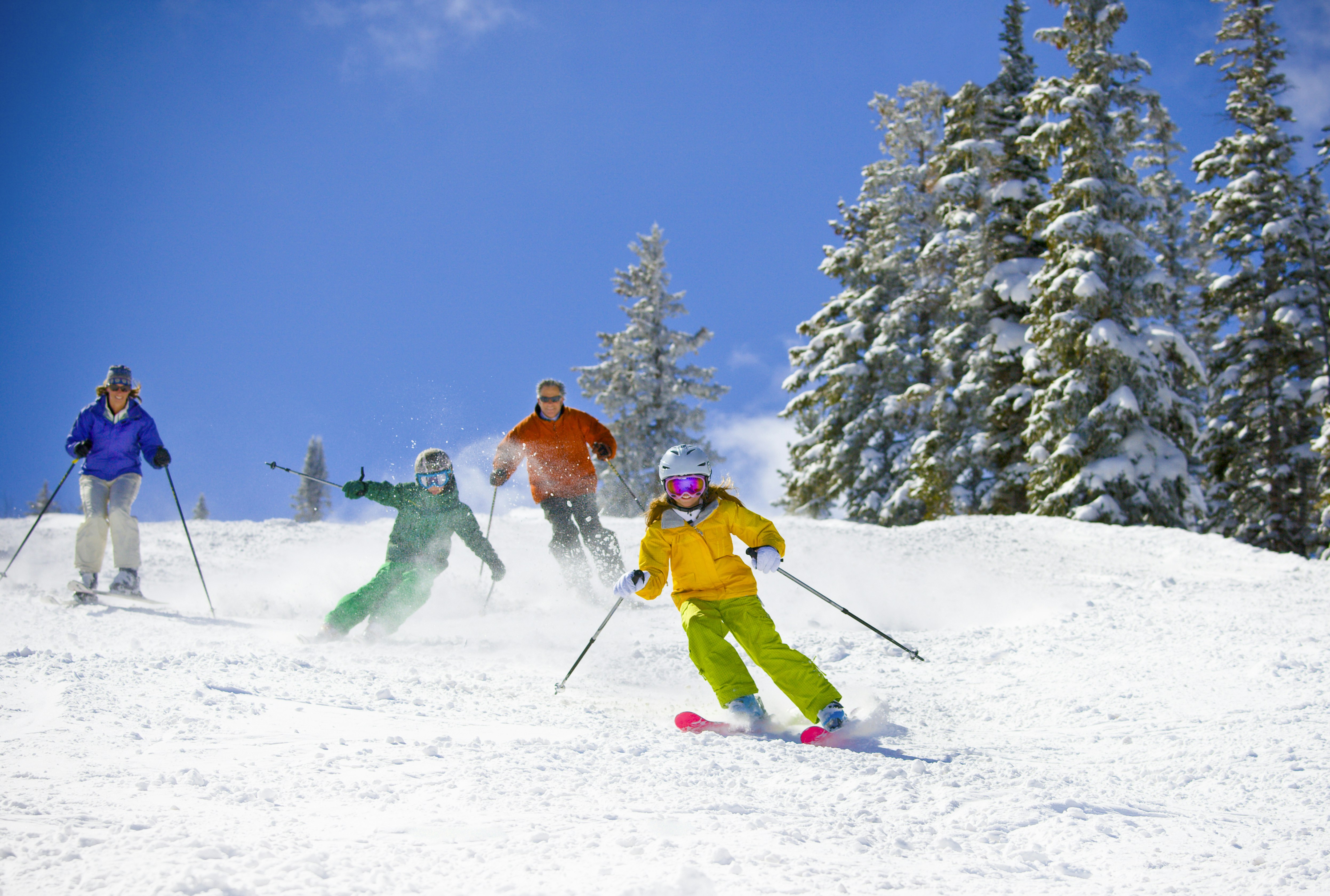 a family of four skis down a powder-white ski run in multi-colored jackets