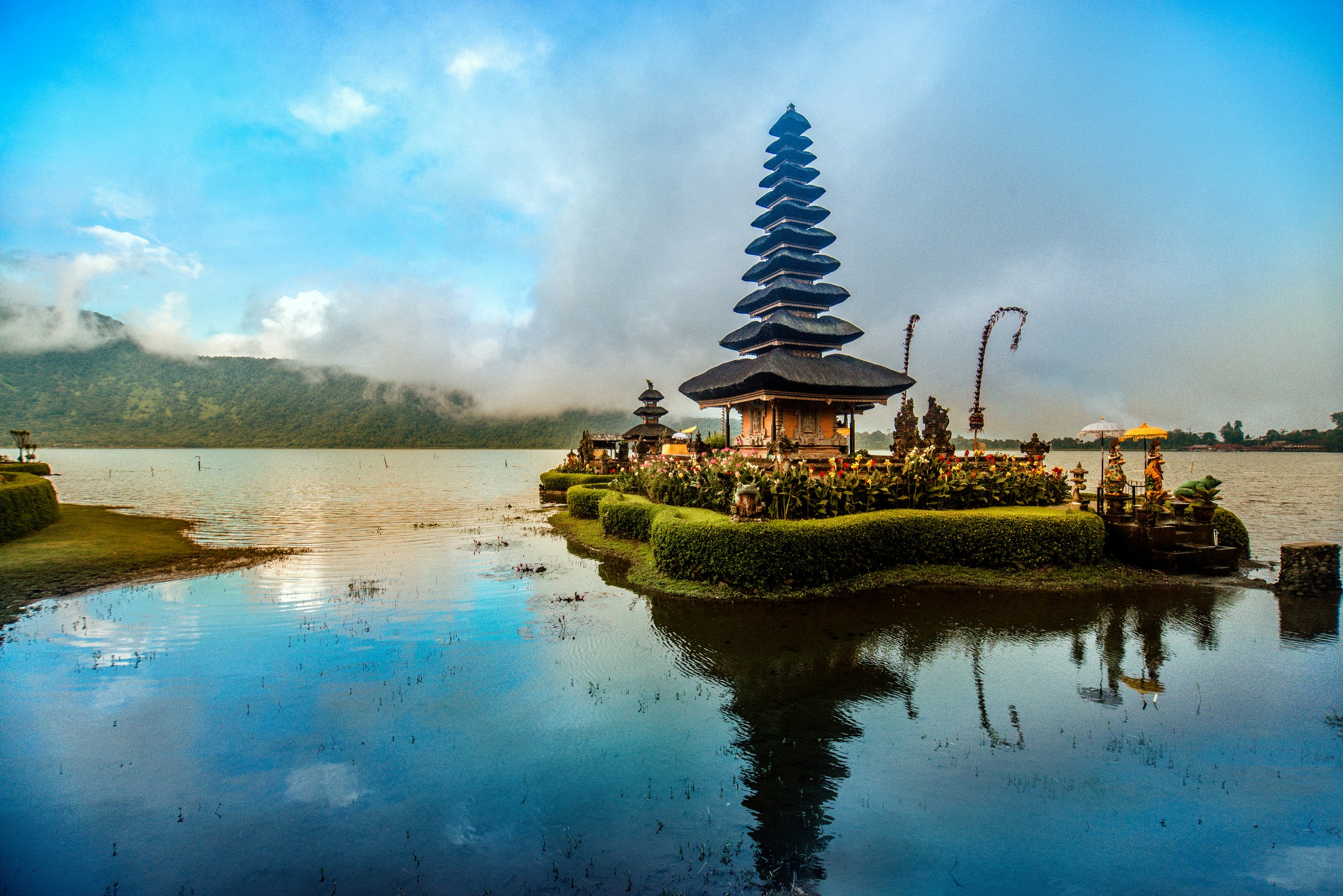 An Indonesian temple appears to float on the water in front of a bright blue sky. 