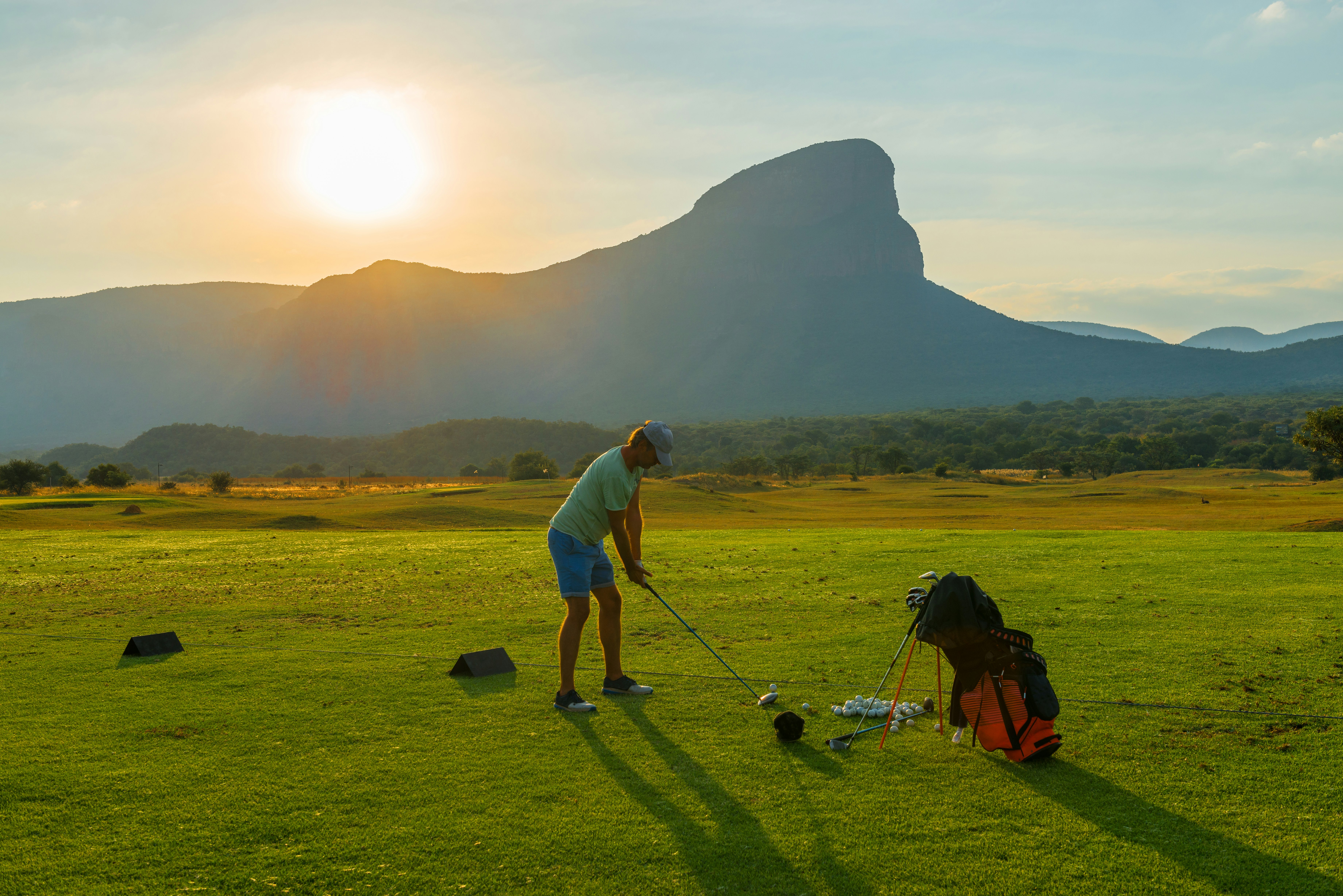 A young male caucasian adult playing golf inside the Entabeni Game Reserve at sunset with a view over the Hanglip or Hanging Lip mountain peak