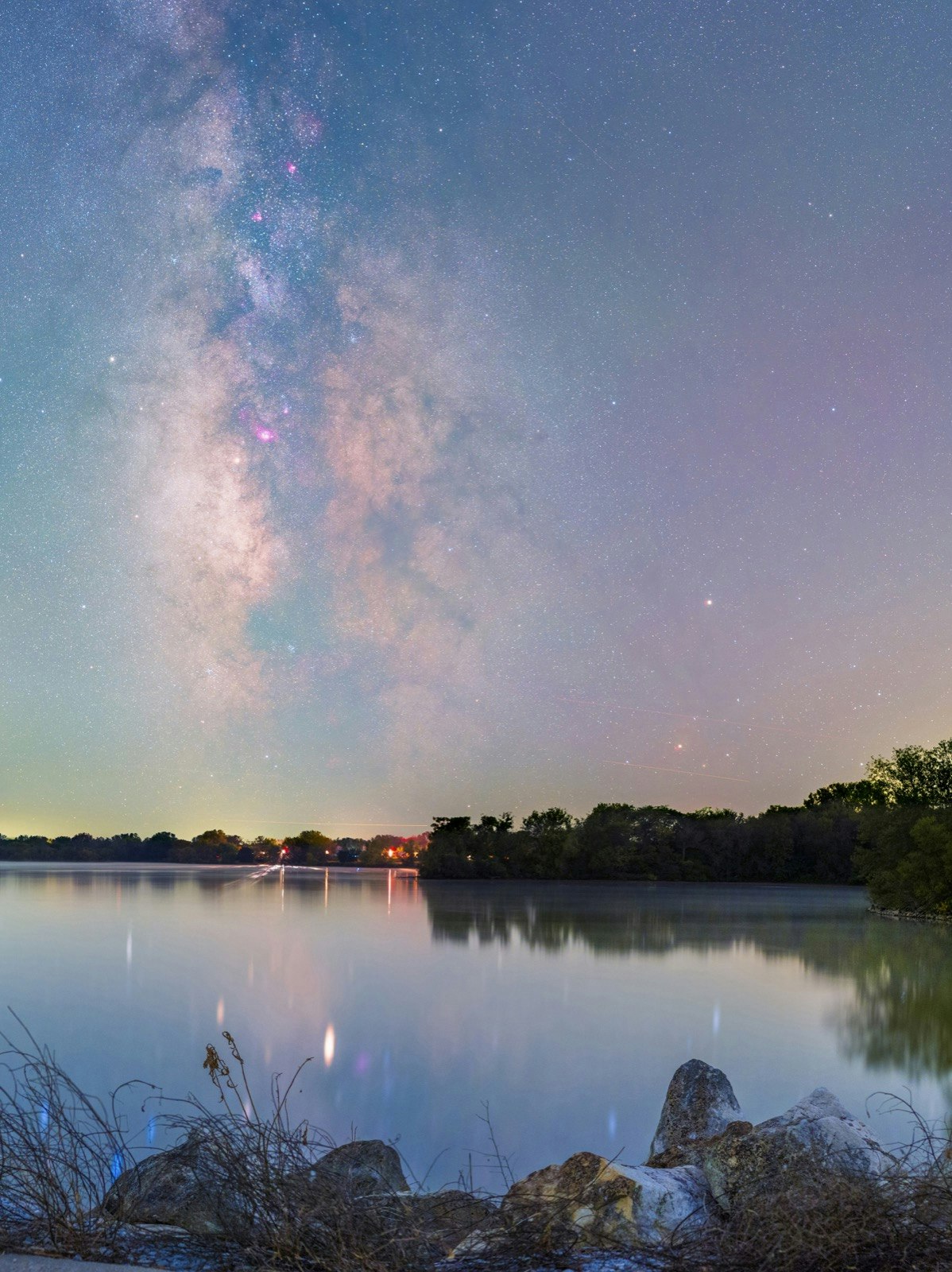A view of the milky way photographed to appear pastel over a lake in Nebraska