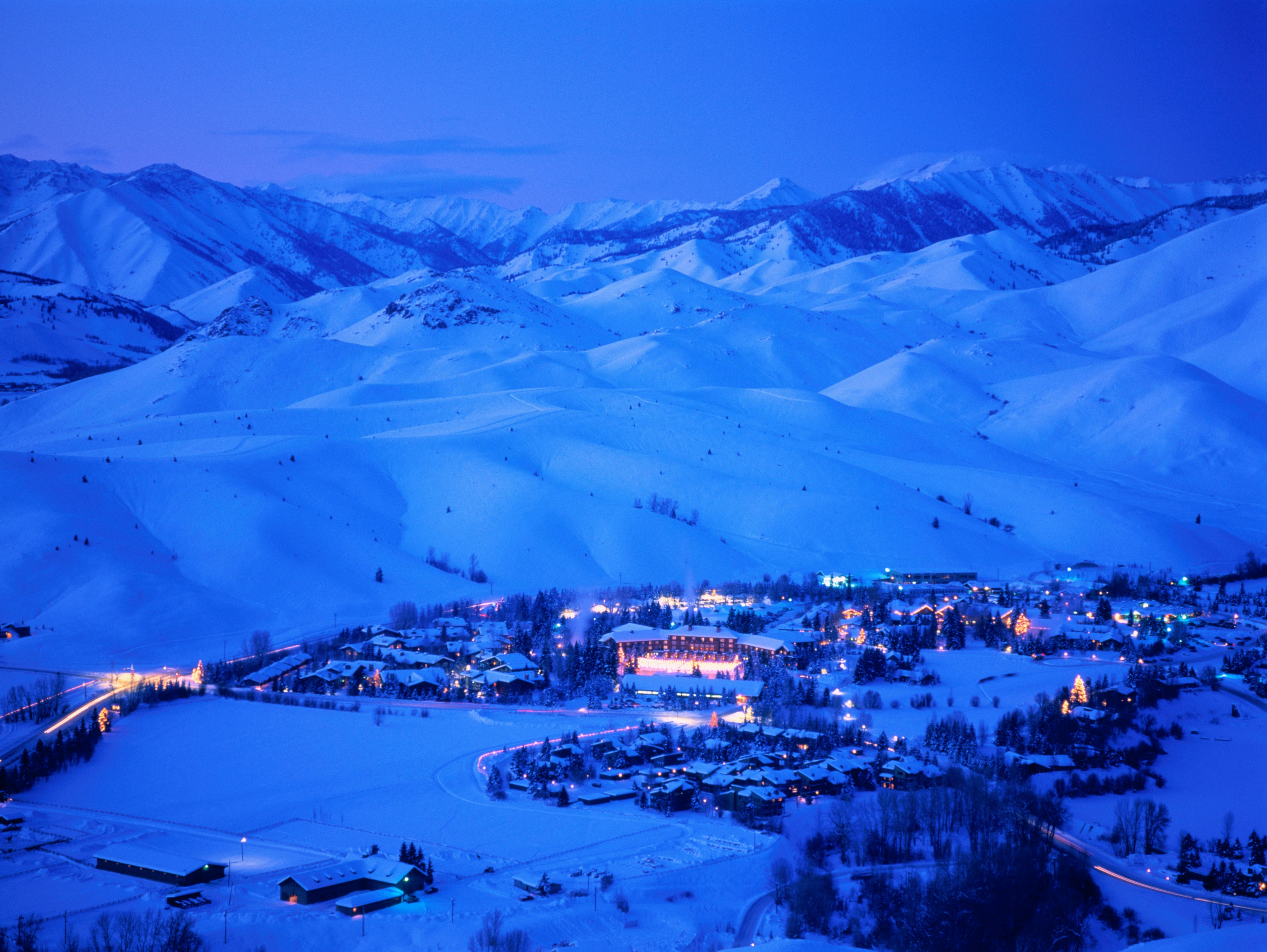 The snowy mountains around Sun Valley Lodge are a deep cobalt blue cast in the early evening. Some of the buildings glow yellow against the snow, but most are a mass of dark geometric shapes against the massif