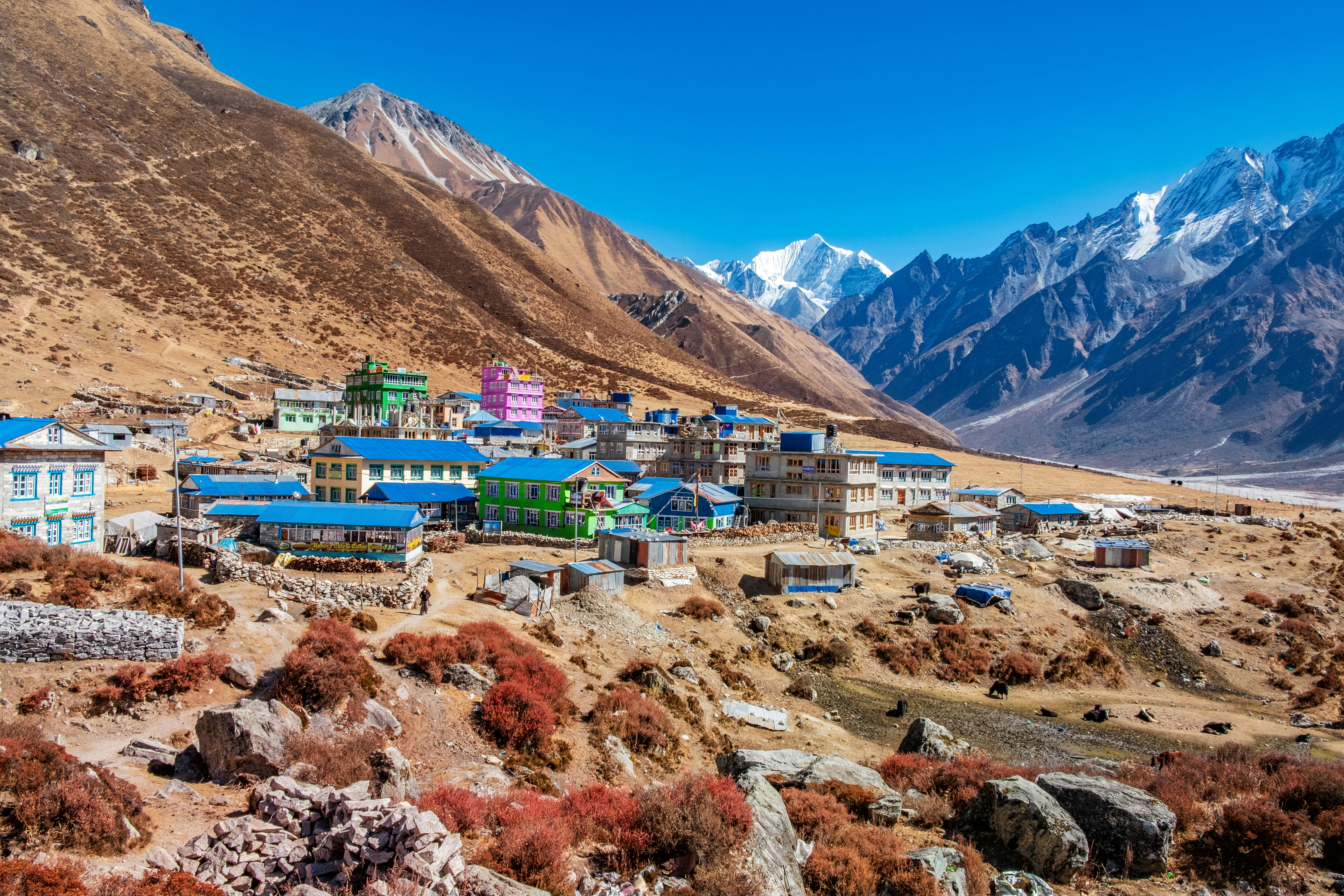 A village with bright blue roofs sits in a valley surrounded by high mountain peaks