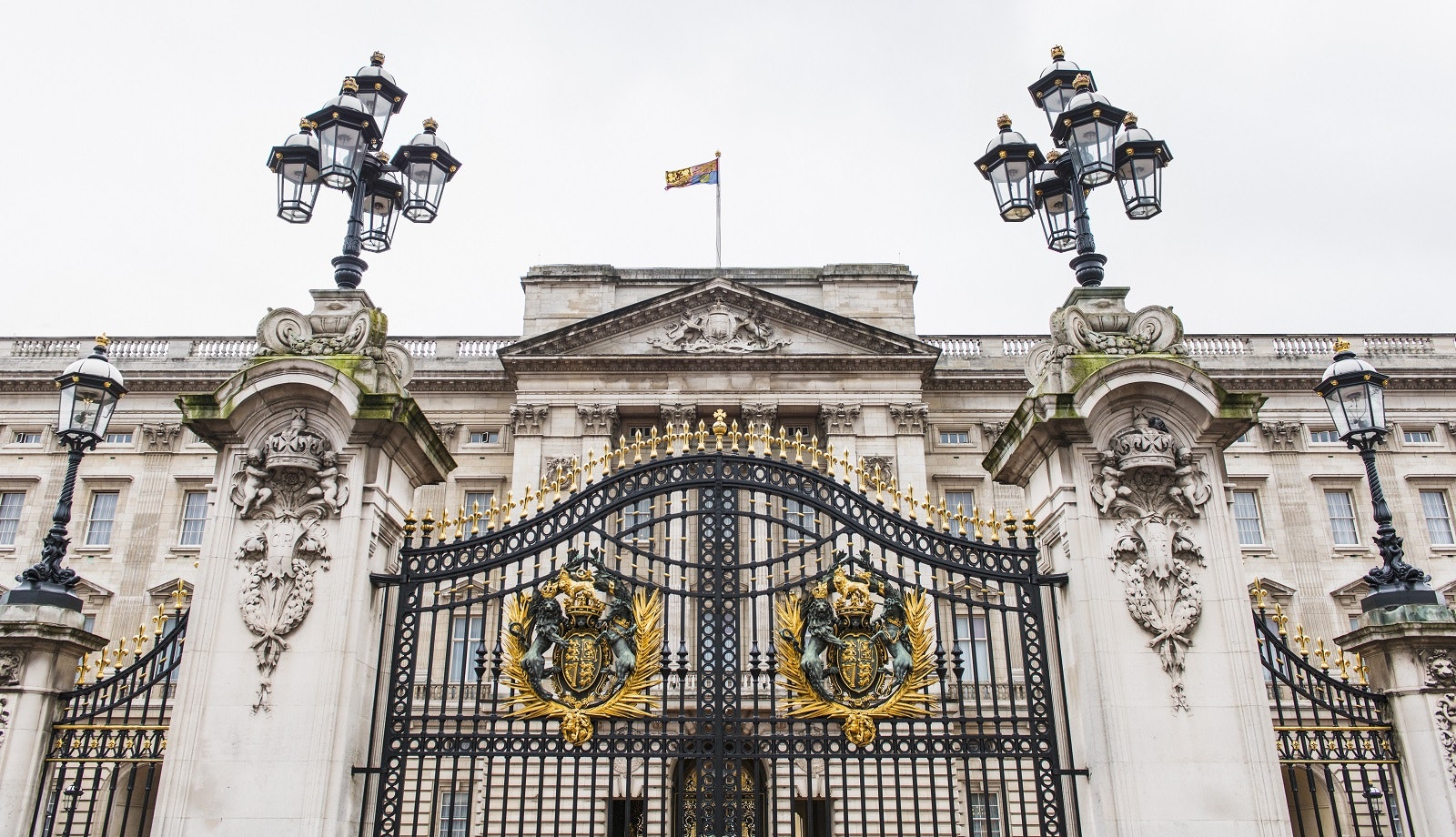 A close-up image of the wrought-iron gates at Buckingham Palace, with the white geometric palace stretching out either side in the background