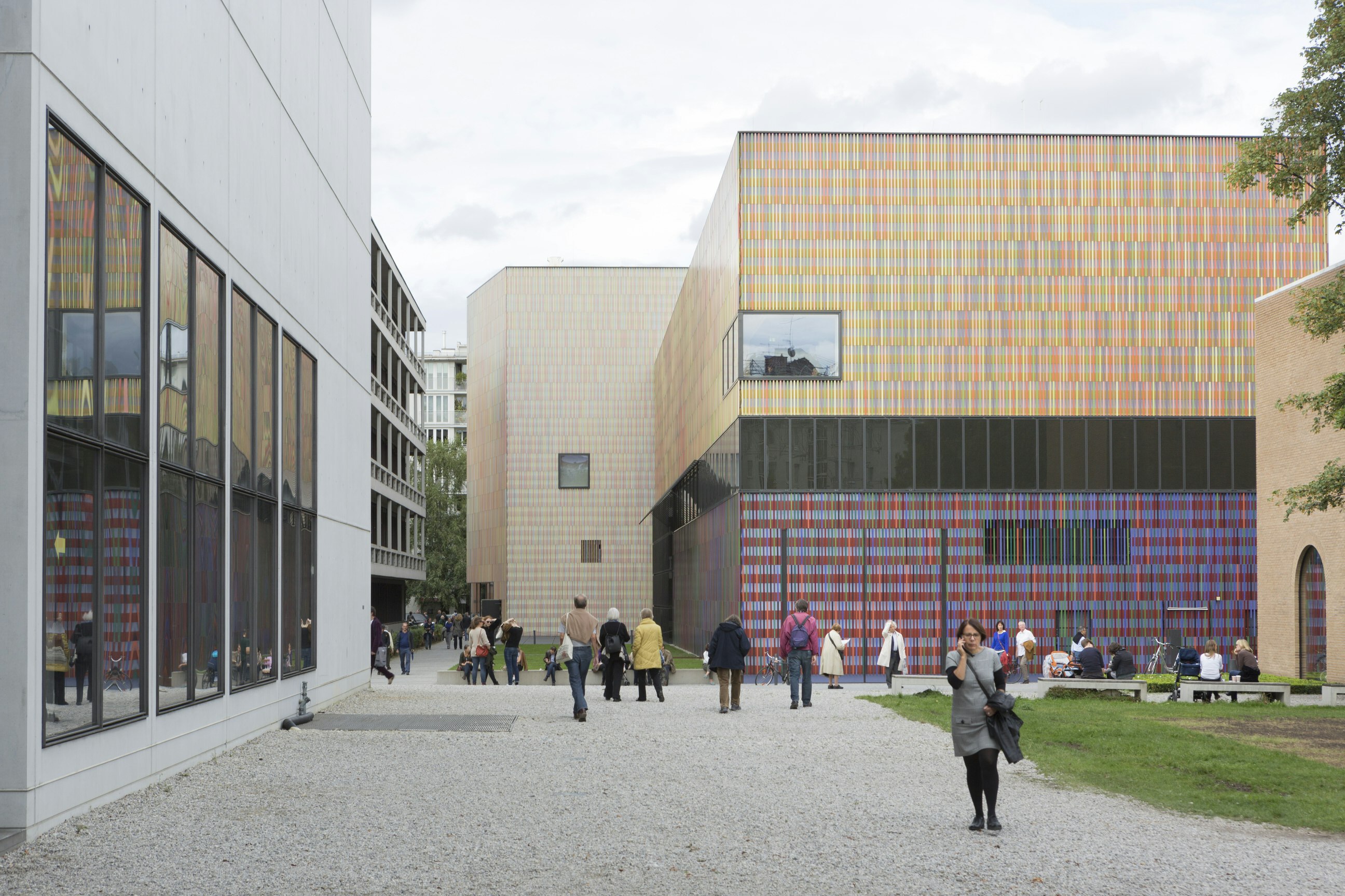 People are milling around in the public realm outside the Museum Brandhorst. The striking modern building is shaped like a cube and is covered in rows of multicoloured rods.