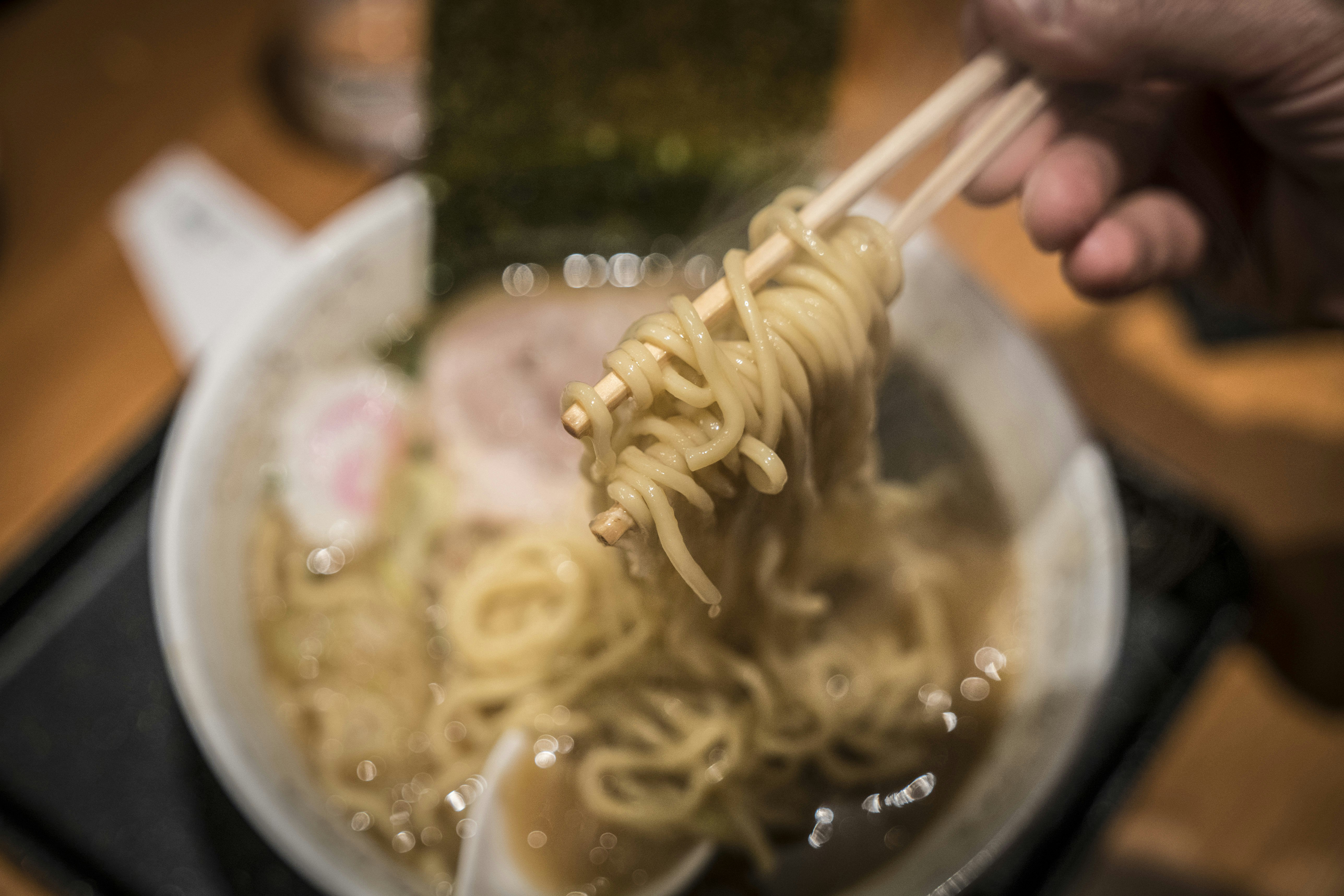 A pair of chopsticks lift a mouthful of noodles from a ramen bowl