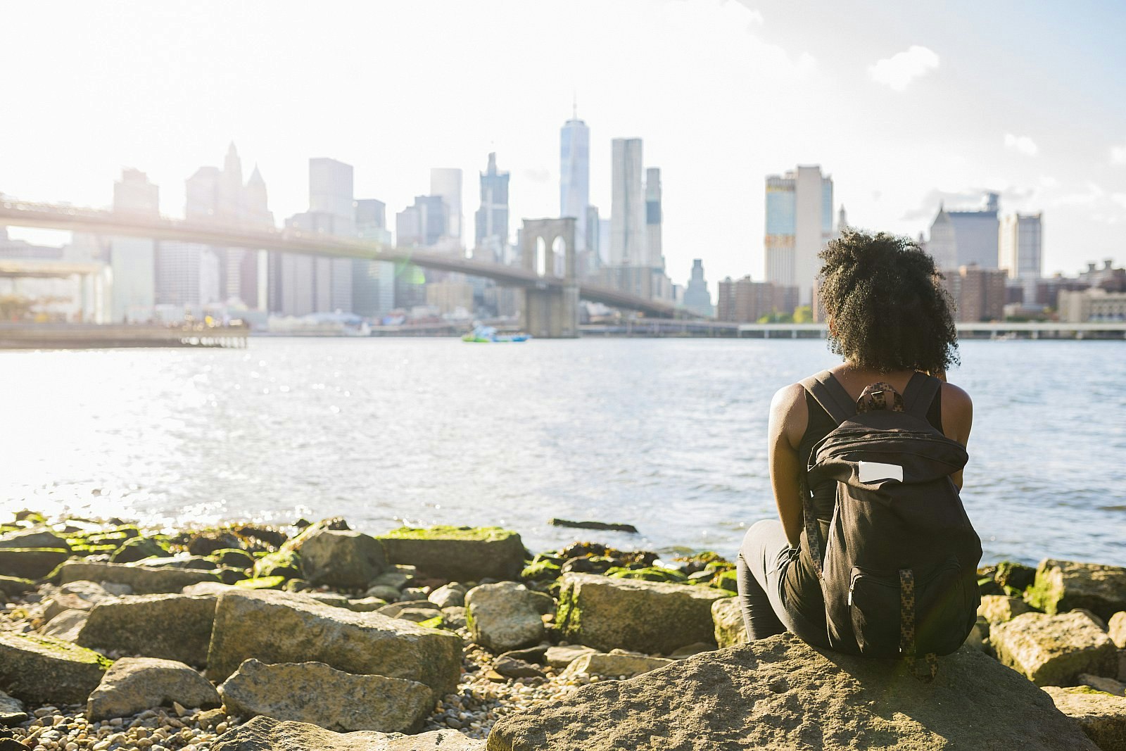 A woman sitting at the waterfront in Brooklyn looking out over the New York City skyline.