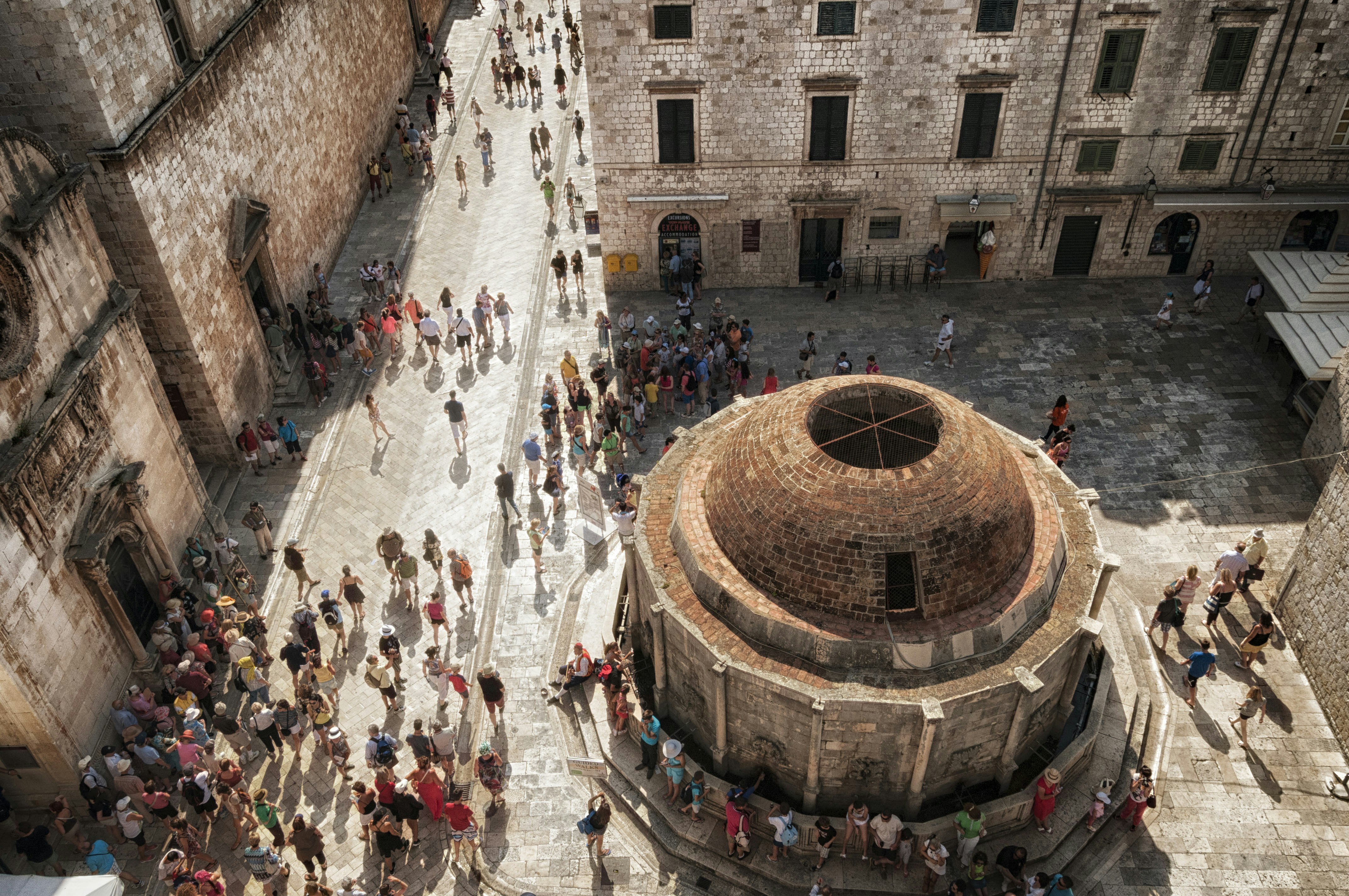 A high-angled shot of colourful crowds of tourists walking through the streets of Dubrovnik's Old Town, which struggles with overtourism issues.