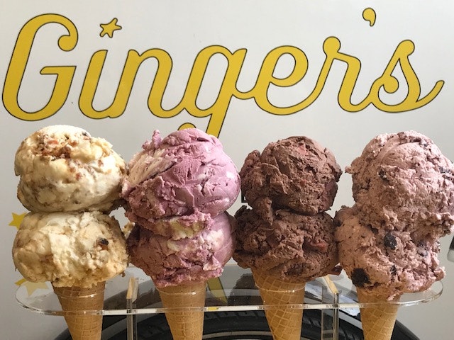 Four double-scoop ice cream cones are placed in a plastic holder in front of a "Ginger's" sign