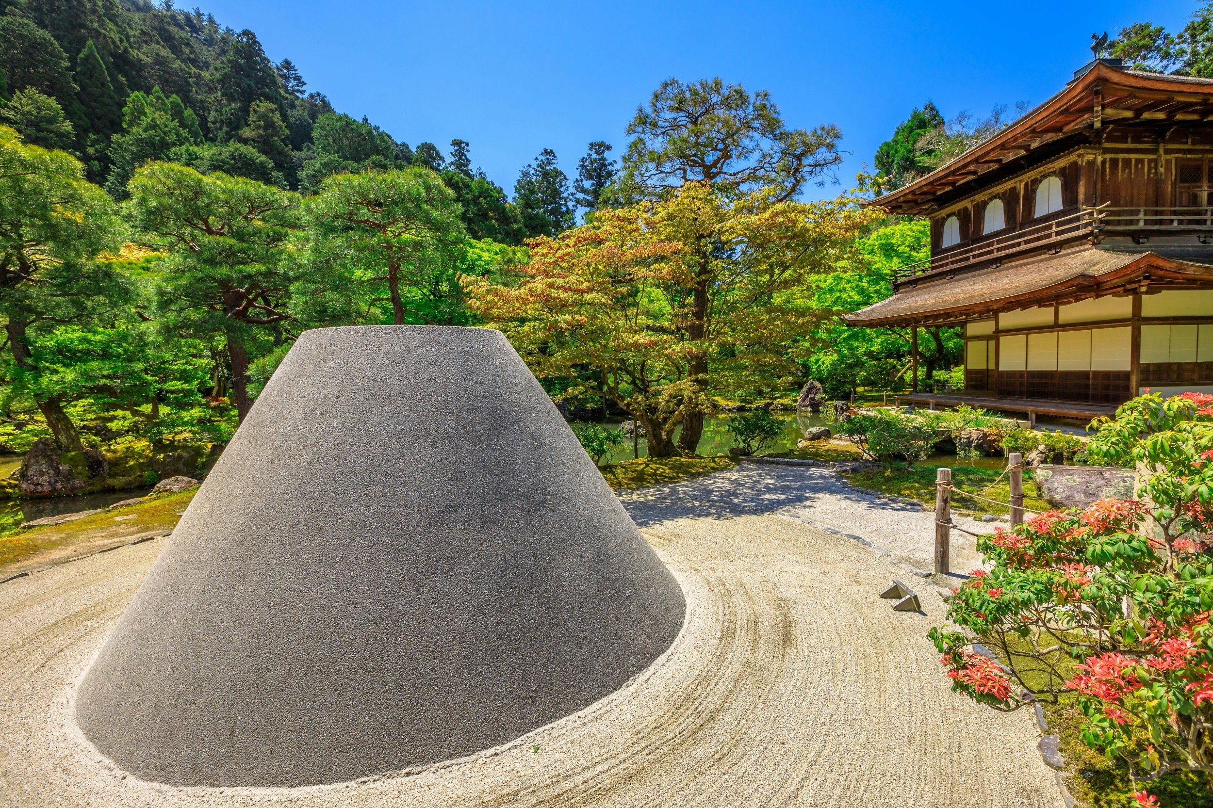 A large conical sand sculpture in a raked Zen garden, with the traditional temple of Ginkaku-ji in the background.