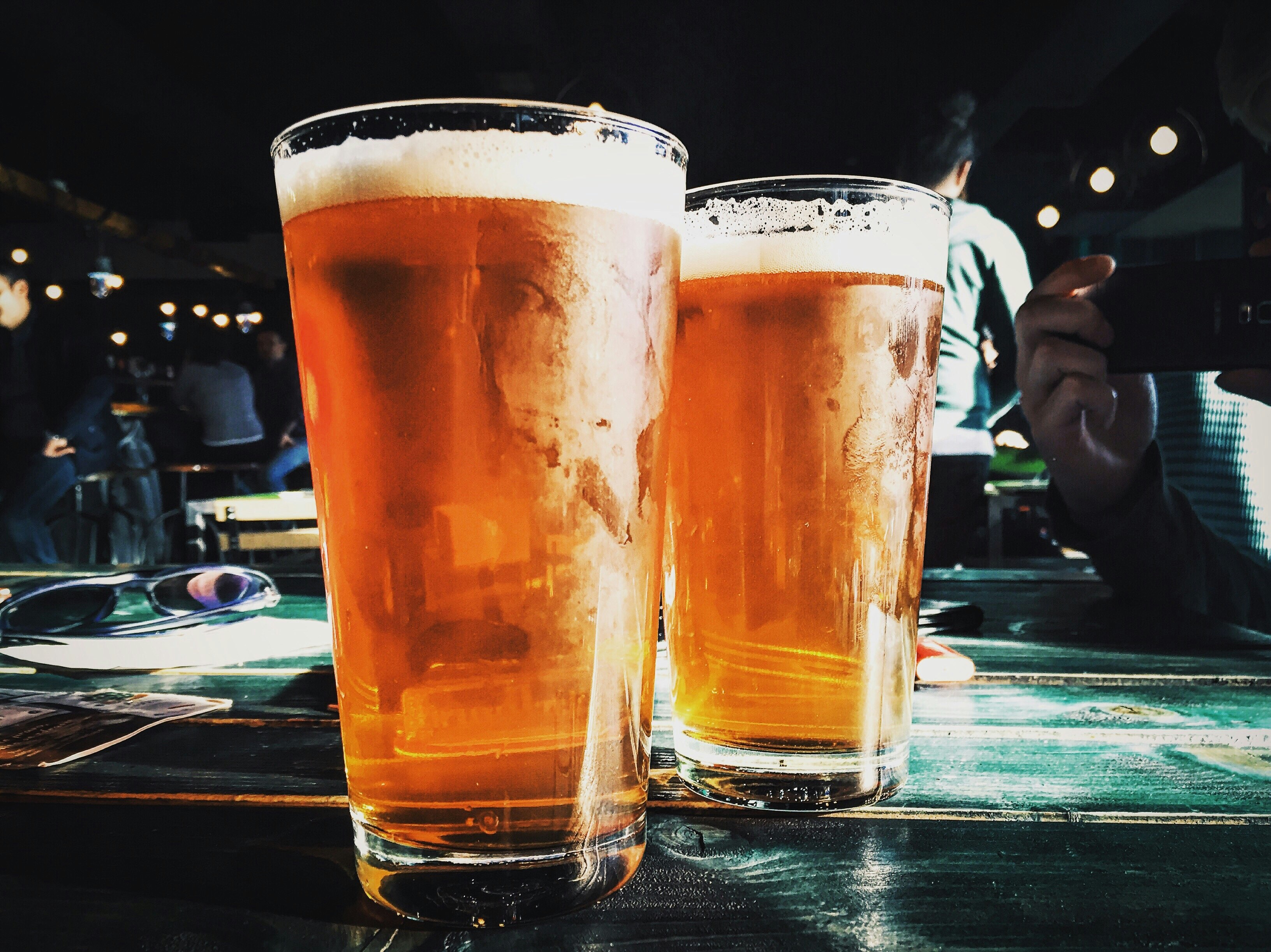 A pair of glasses filled with beer rest on a table in a crowded bar; NFL bars