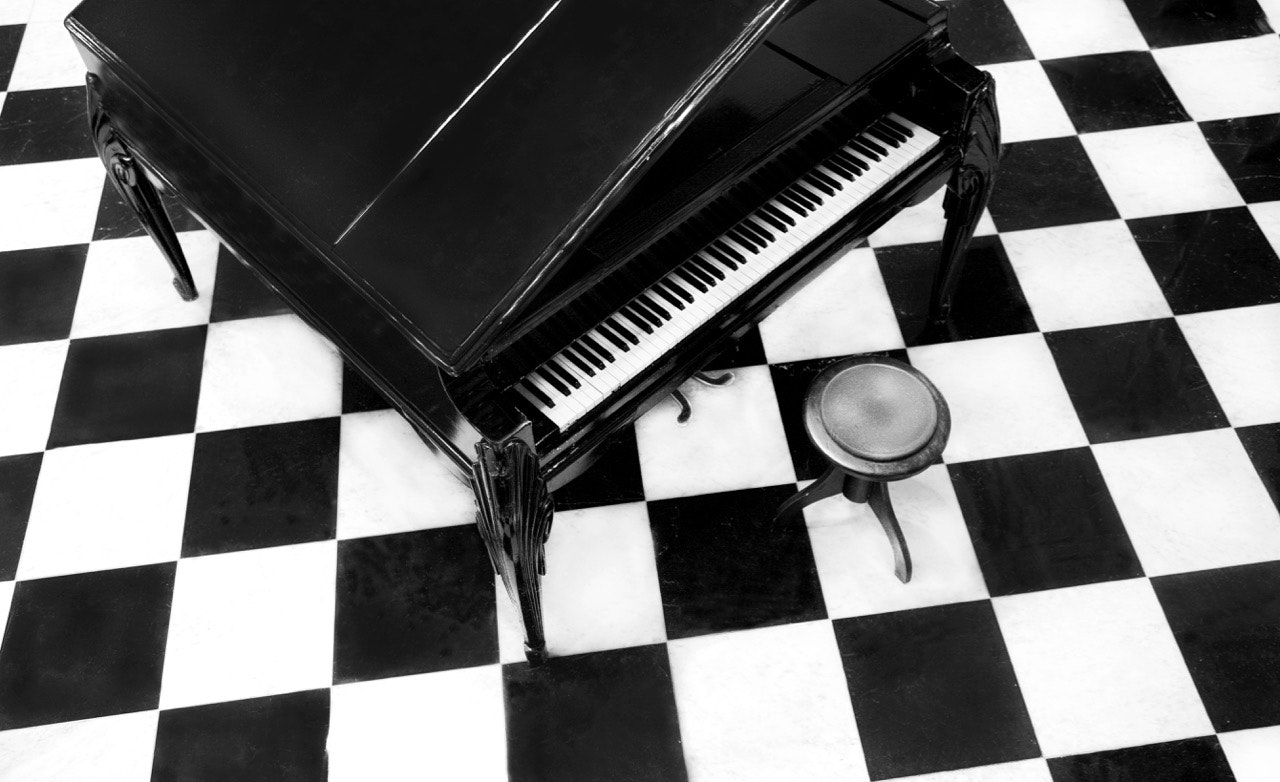 Overview of a grand piano on a checkered floor. 