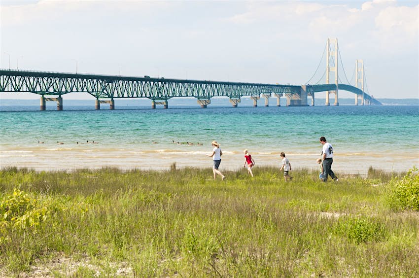 A family walks along the lake shore with the Mackinac bridge in the background; Great Lakes road trip